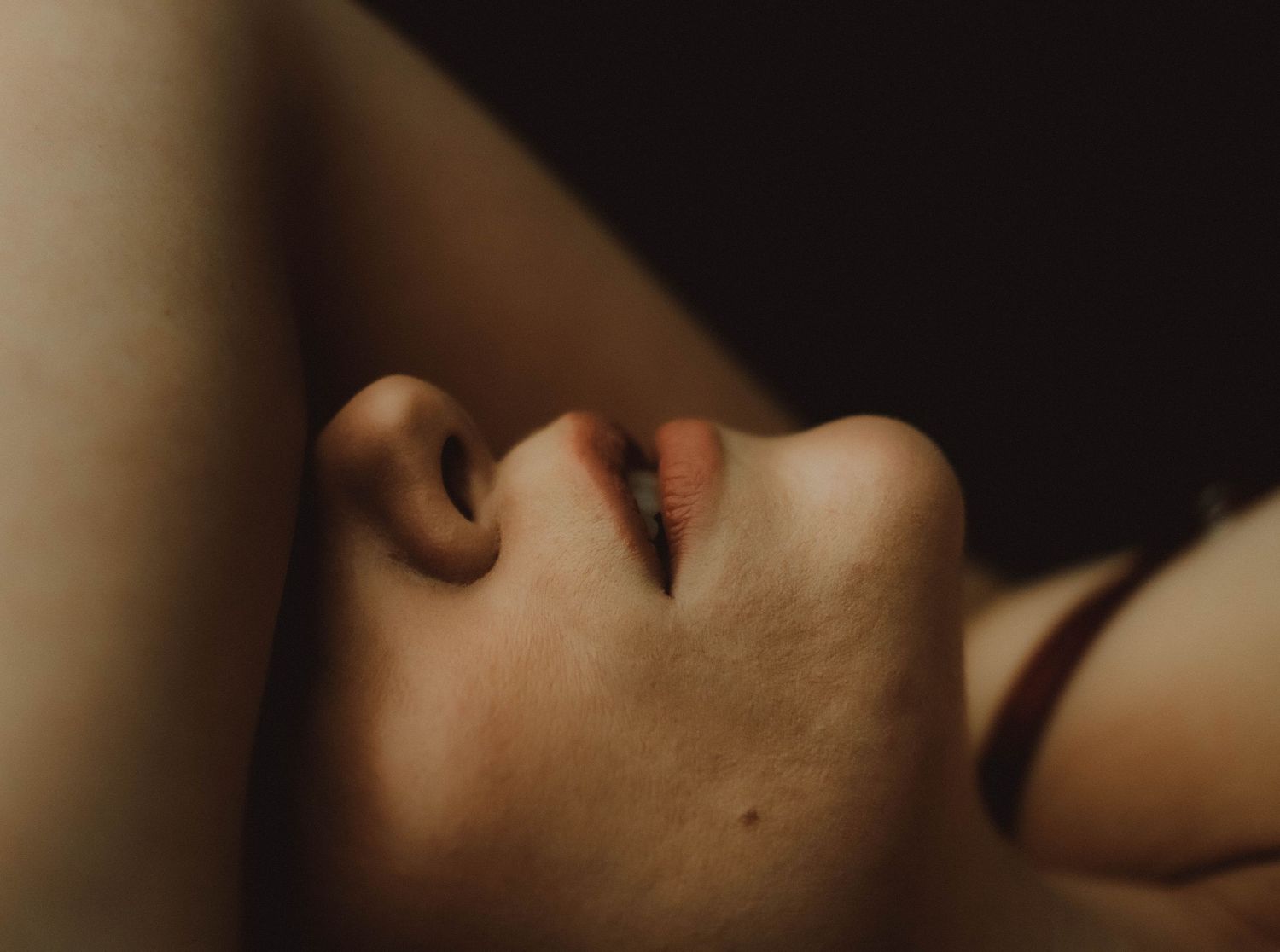Close-up portrait of a person's face tilted back, highlighting their nose and lips in warm, dramatic lighting.