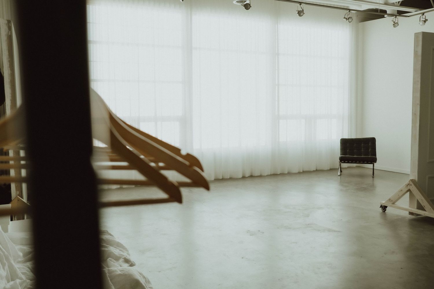Minimalist photography studio interior with large white curtains, concrete floors, and wooden chairs.