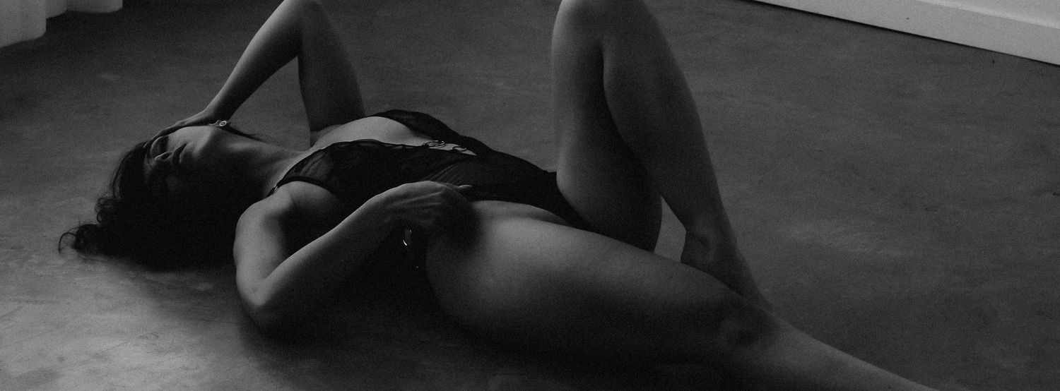Black and white artistic photo of a woman lying on the floor in a graceful pose wearing dark lingerie.