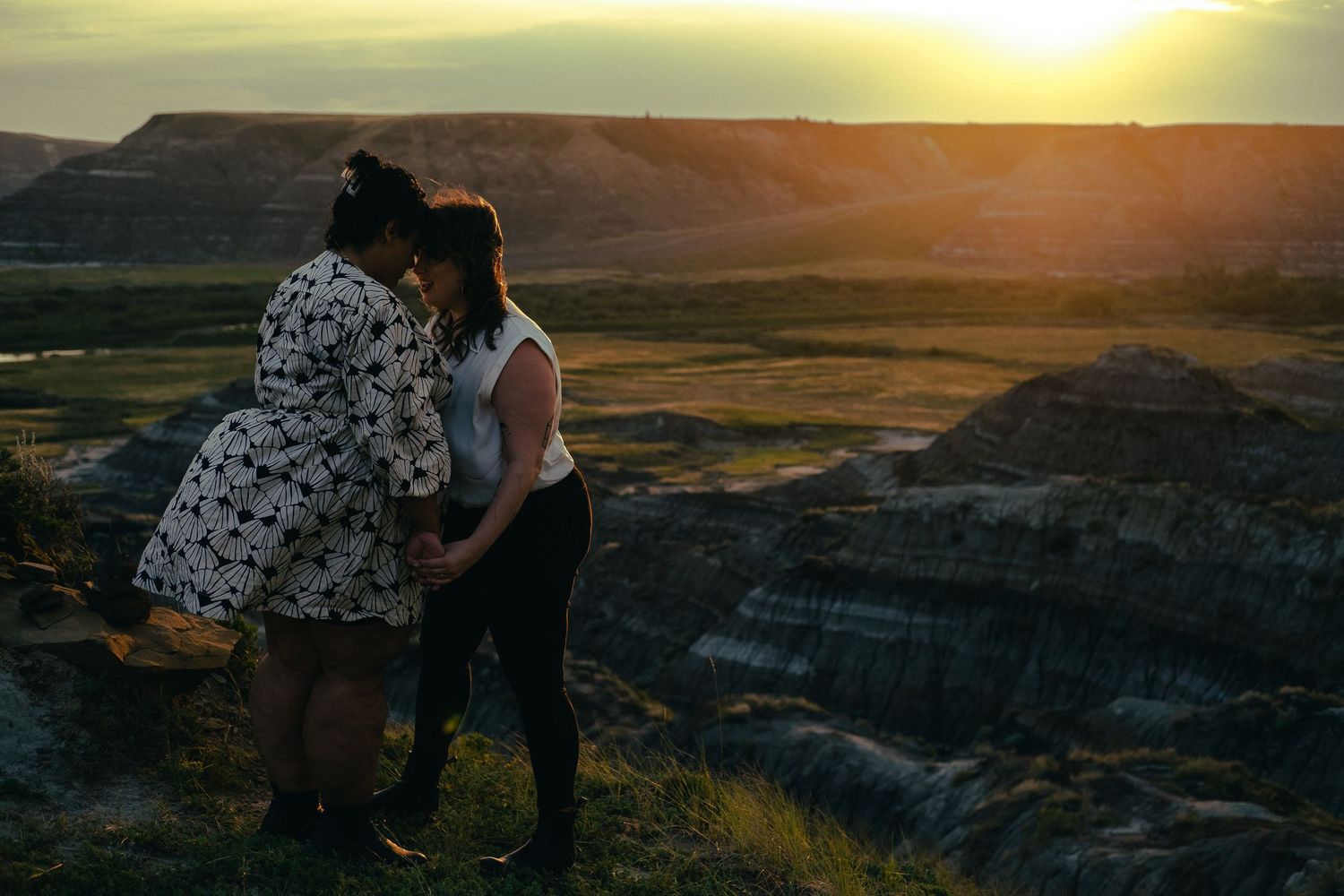Two women holding hands and sharing an intimate moment at sunset overlooking a stunning canyon vista.