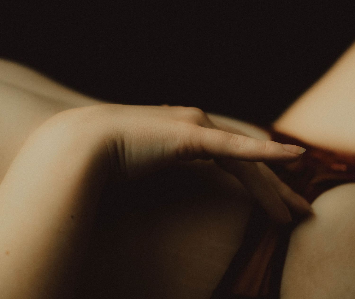 Close-up of a hand resting gently on bare skin in soft, moody lighting with dark background.