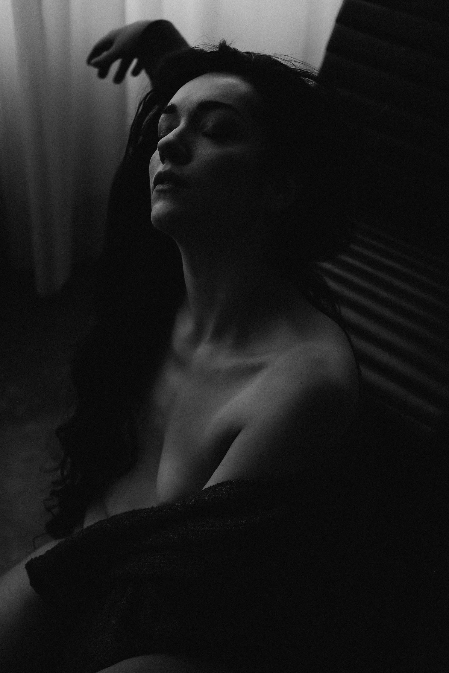 Black and white artistic portrait of a woman with closed eyes, hand in hair, in dramatic low-key lighting.