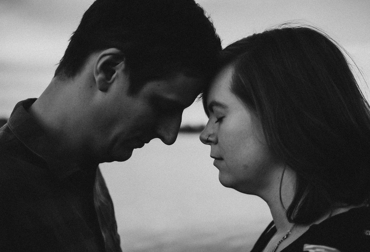 Black and white photo of a romantic couple leaning foreheads together in an intimate moment outdoors.