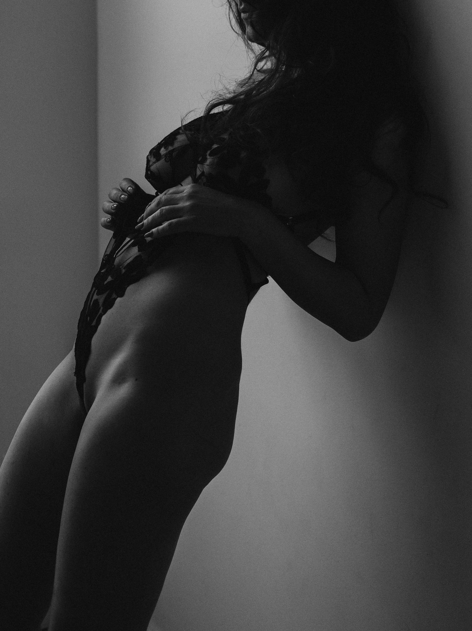 Black and white silhouette of a woman's curved figure holding lace lingerie against a light background.