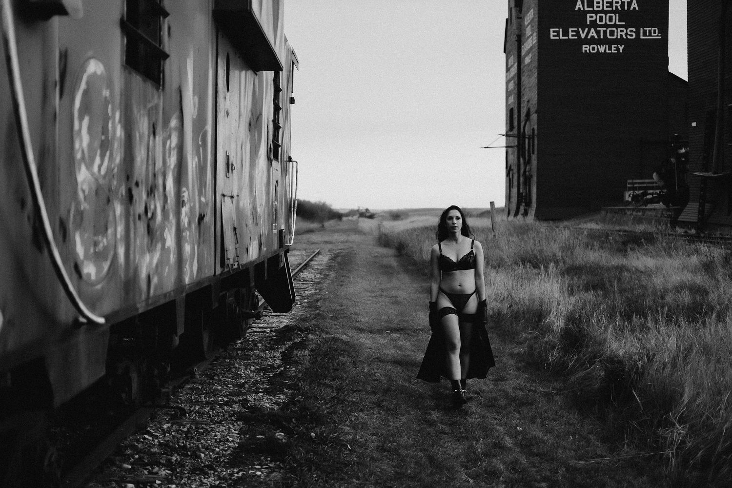 Black and white photo of a woman in lingerie walking between train cars near Alberta Pool Elevators in Rowley.
