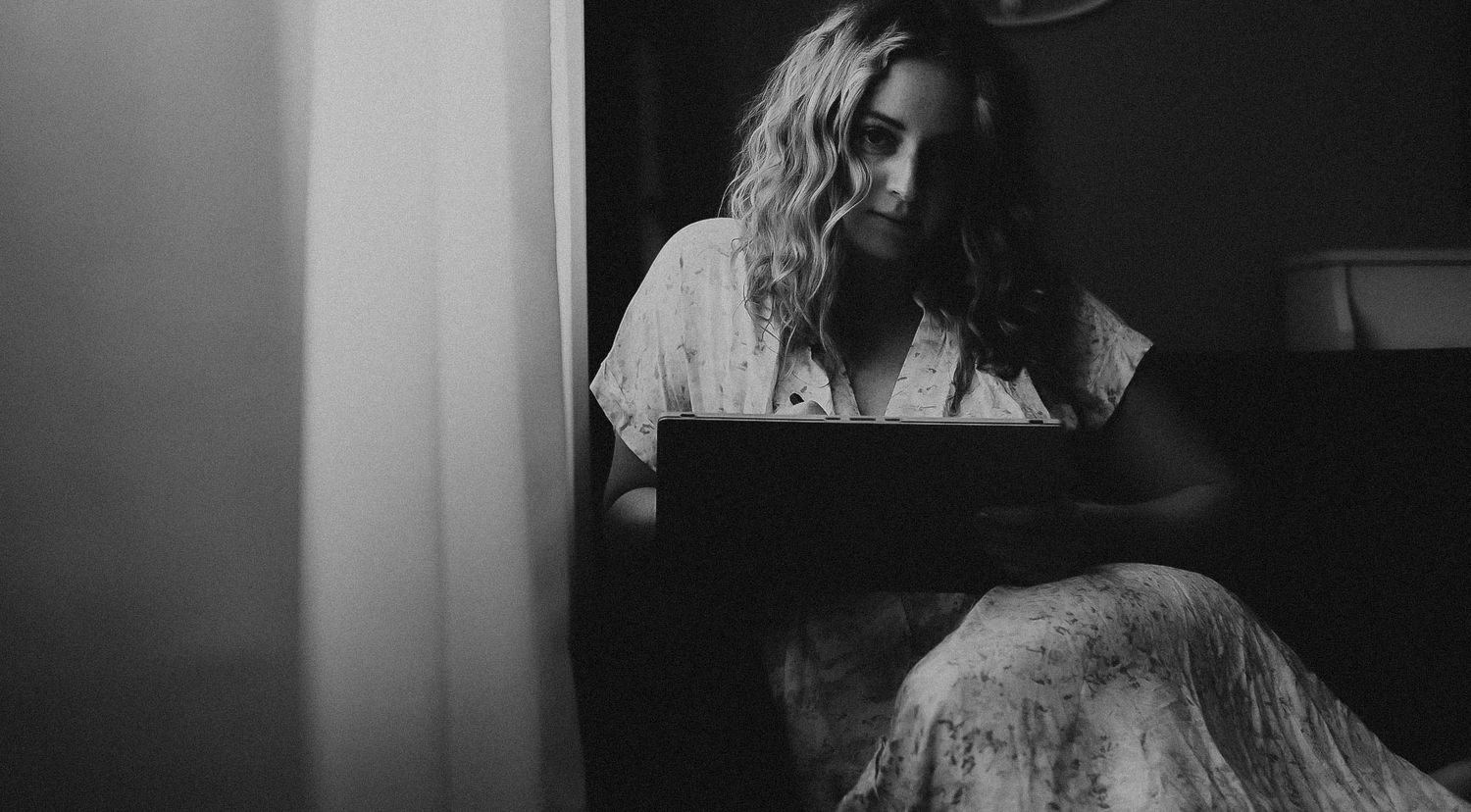 Black and white photo of a woman with curly hair sitting and reading a book in a dimly lit room.