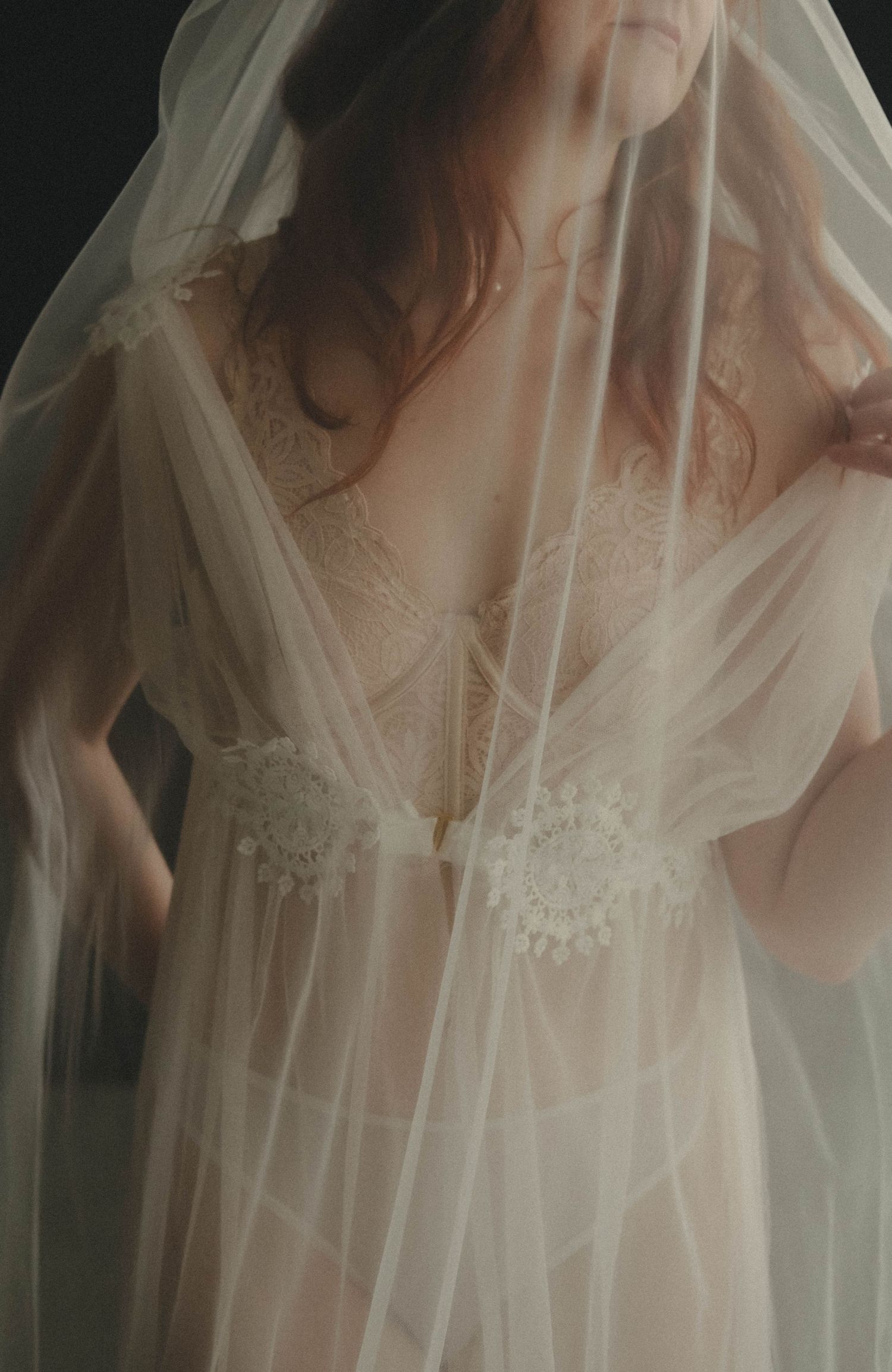 Bride wearing sheer tulle veil and lace lingerie gown in an ethereal bridal boudoir portrait.