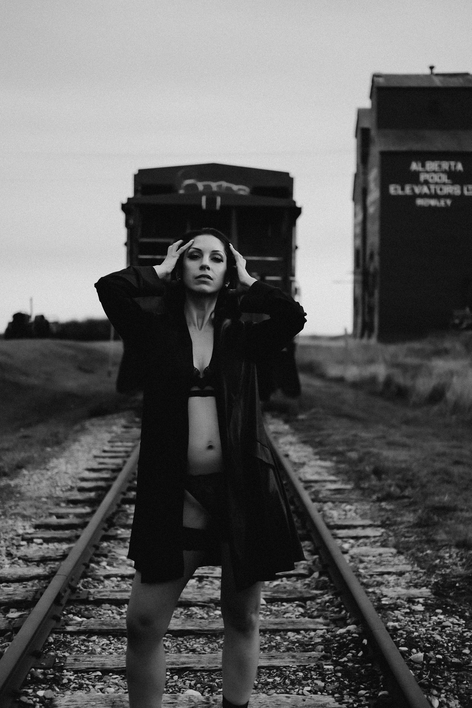 Black and white photo of a woman standing on railroad tracks near Alberta Pool Elevators grain elevator.