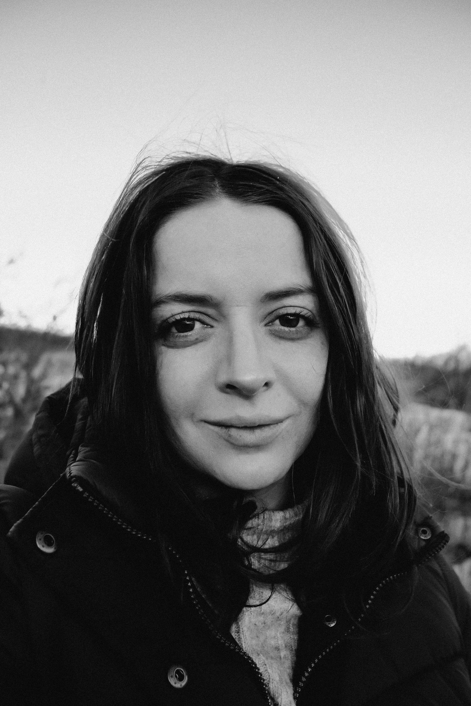 Black and white portrait of a young woman with dark hair wearing a jacket outdoors.