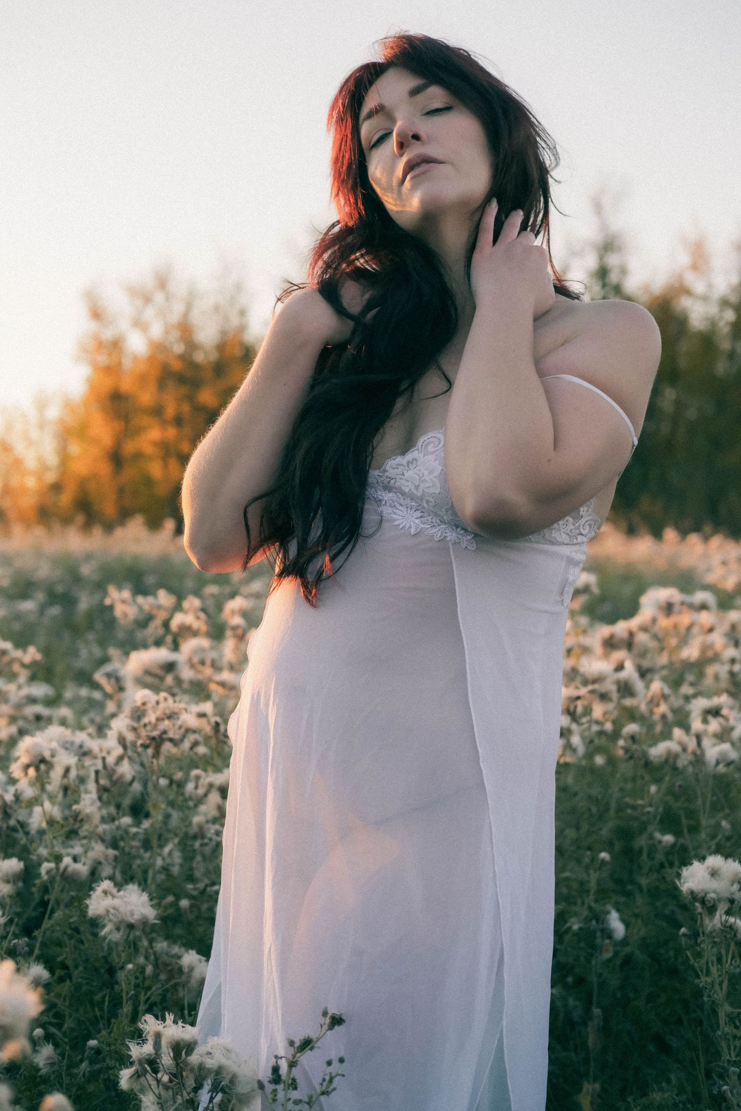 Woman in white dress standing in flower field at golden hour sunset.