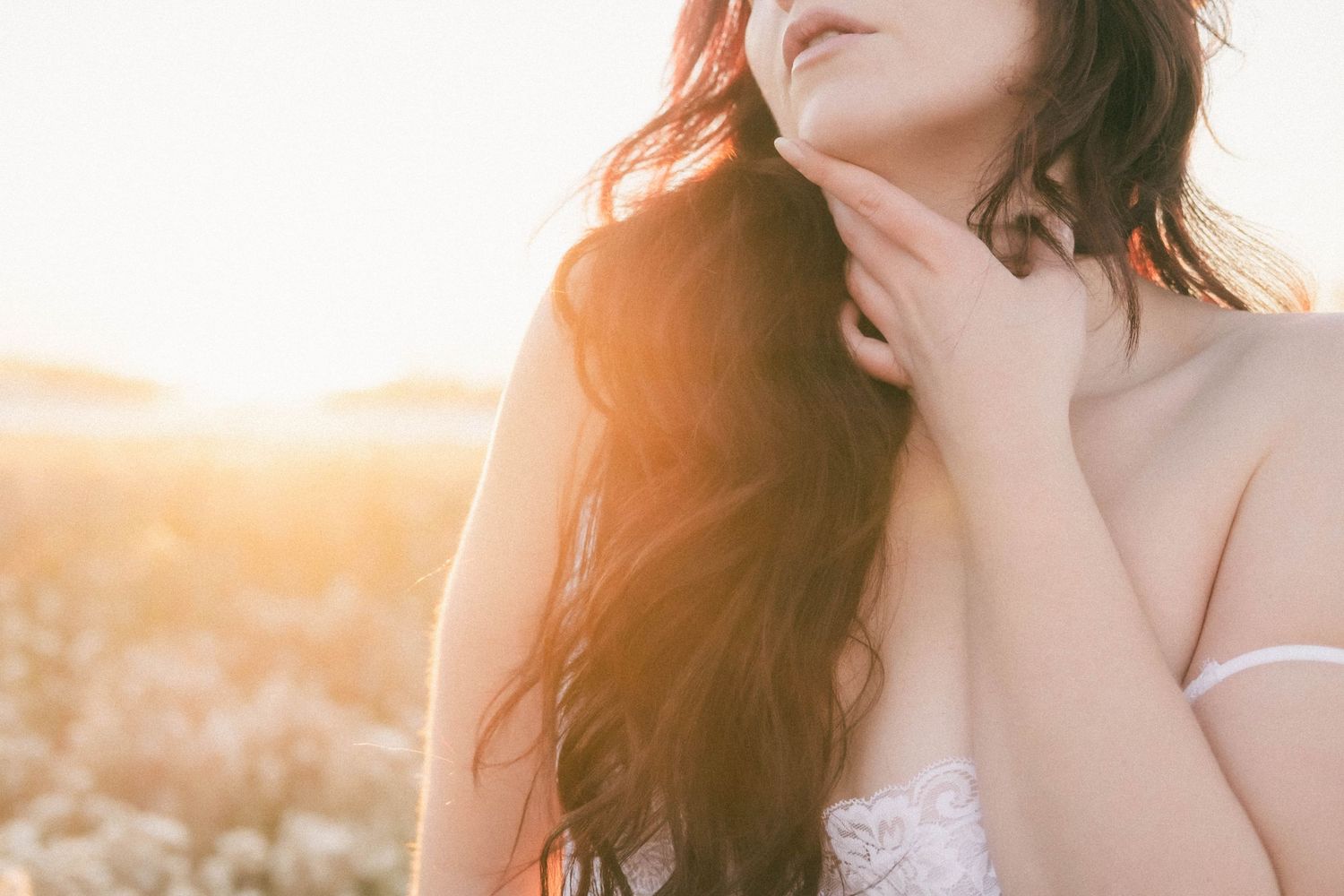 Young woman with long brown hair touching her neck in golden sunset light outdoors.