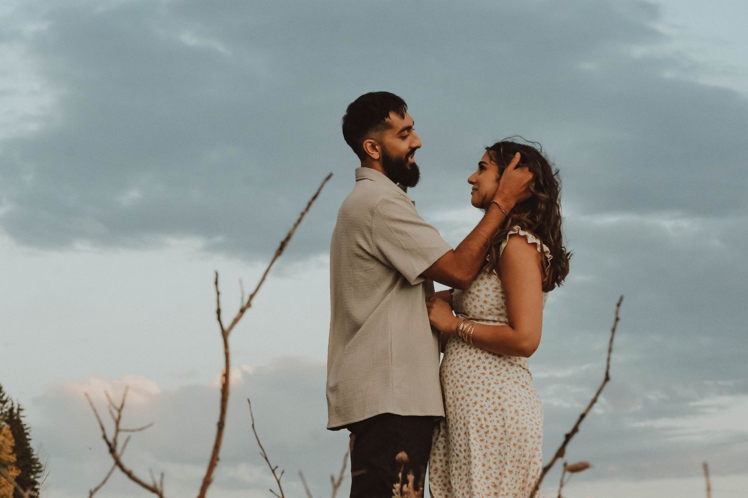 A couple shares a romantic moment outdoors under a cloudy sky, the man gently holding the woman's face.