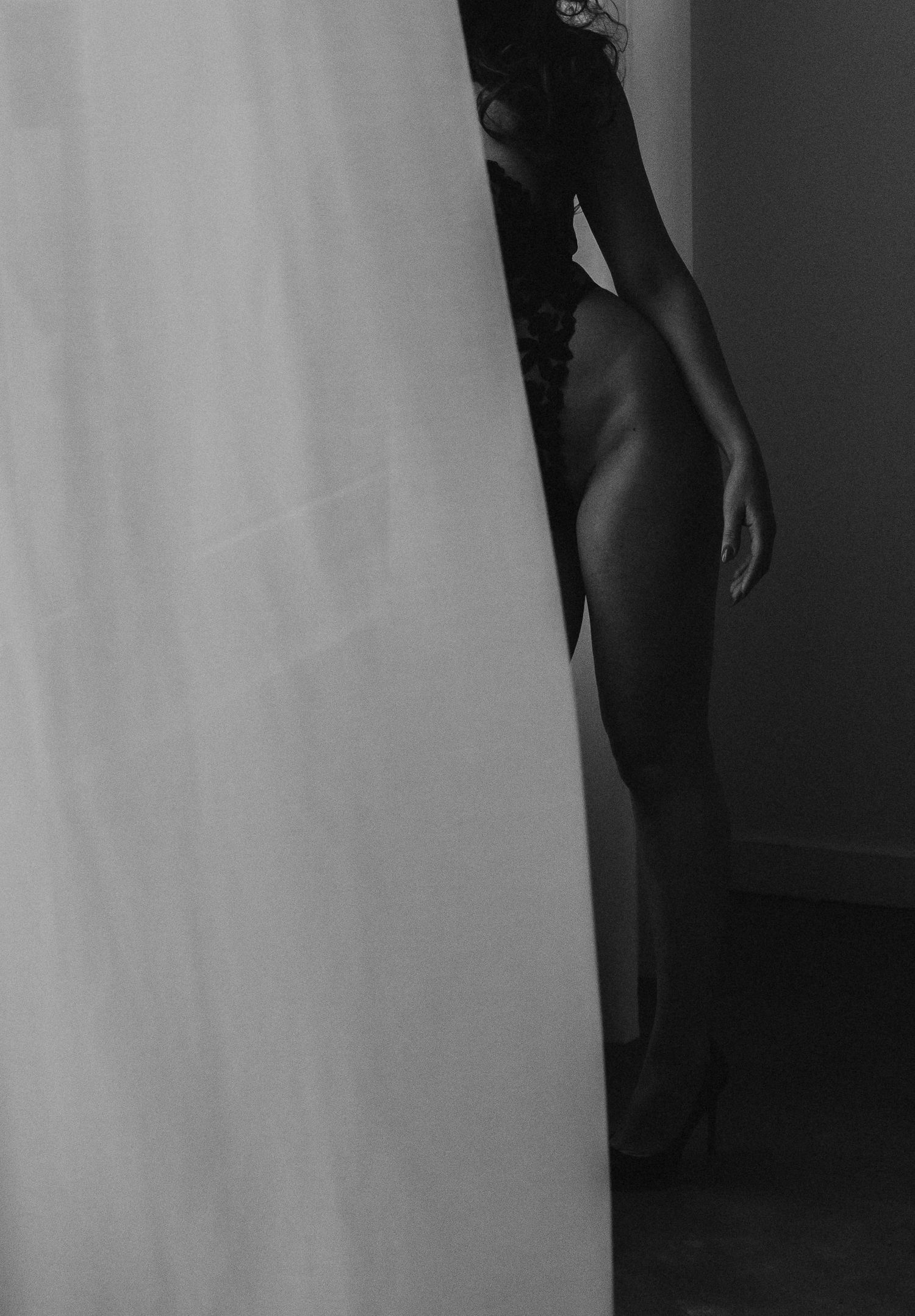 Black and white artistic shot of a woman partially hidden behind a sheer white curtain in lingerie.