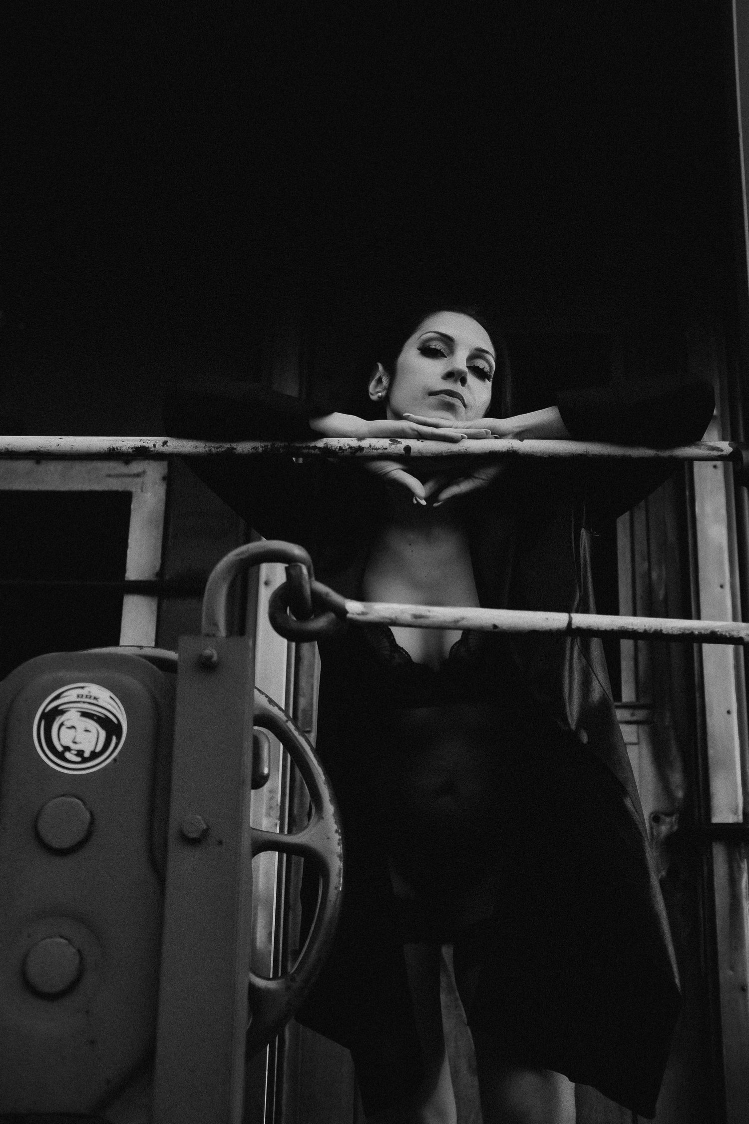 Black and white photo of a woman leaning on metal railings in a dark industrial setting.