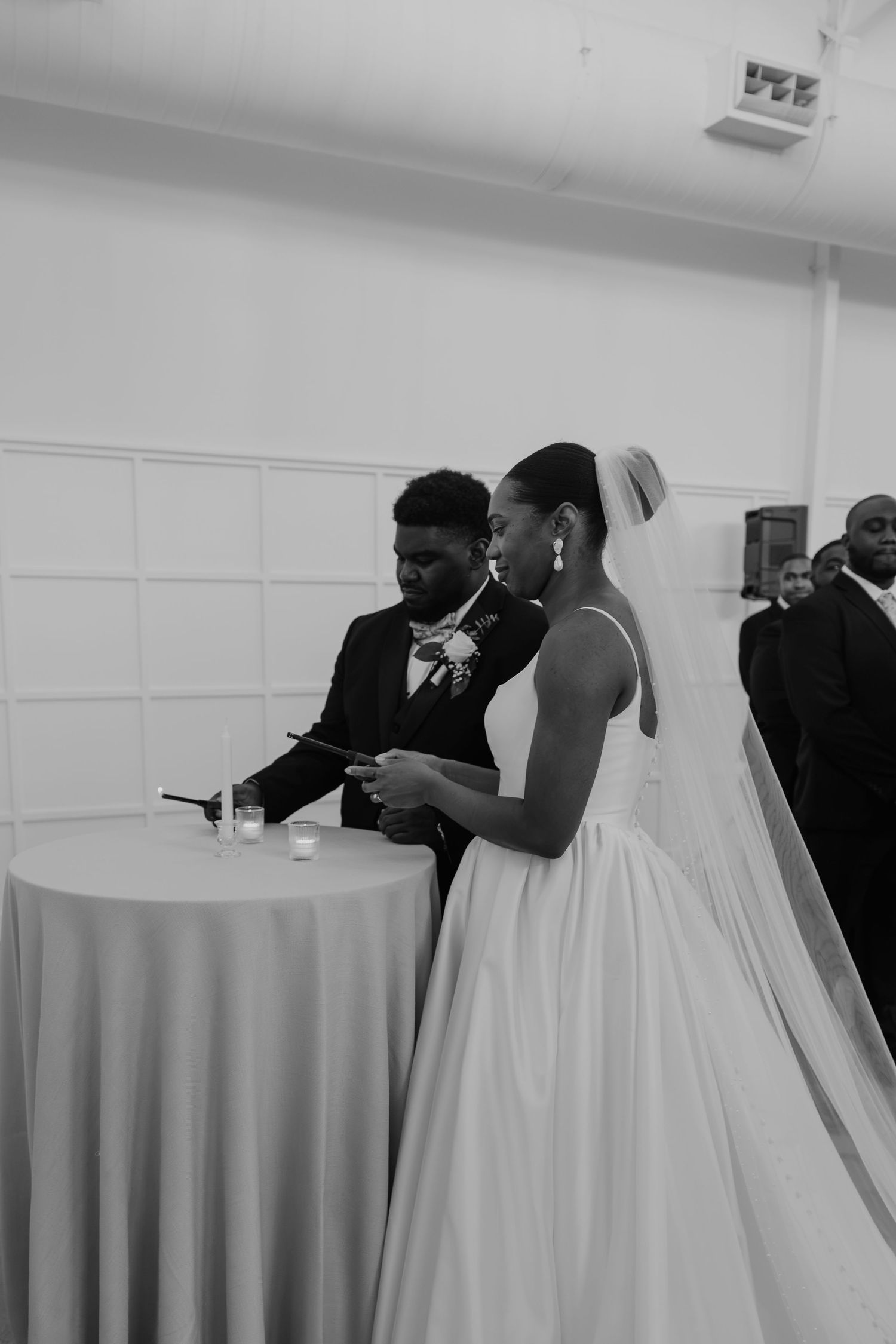 Black and white photo of a bride and groom signing wedding documents at a draped table during their ceremony.