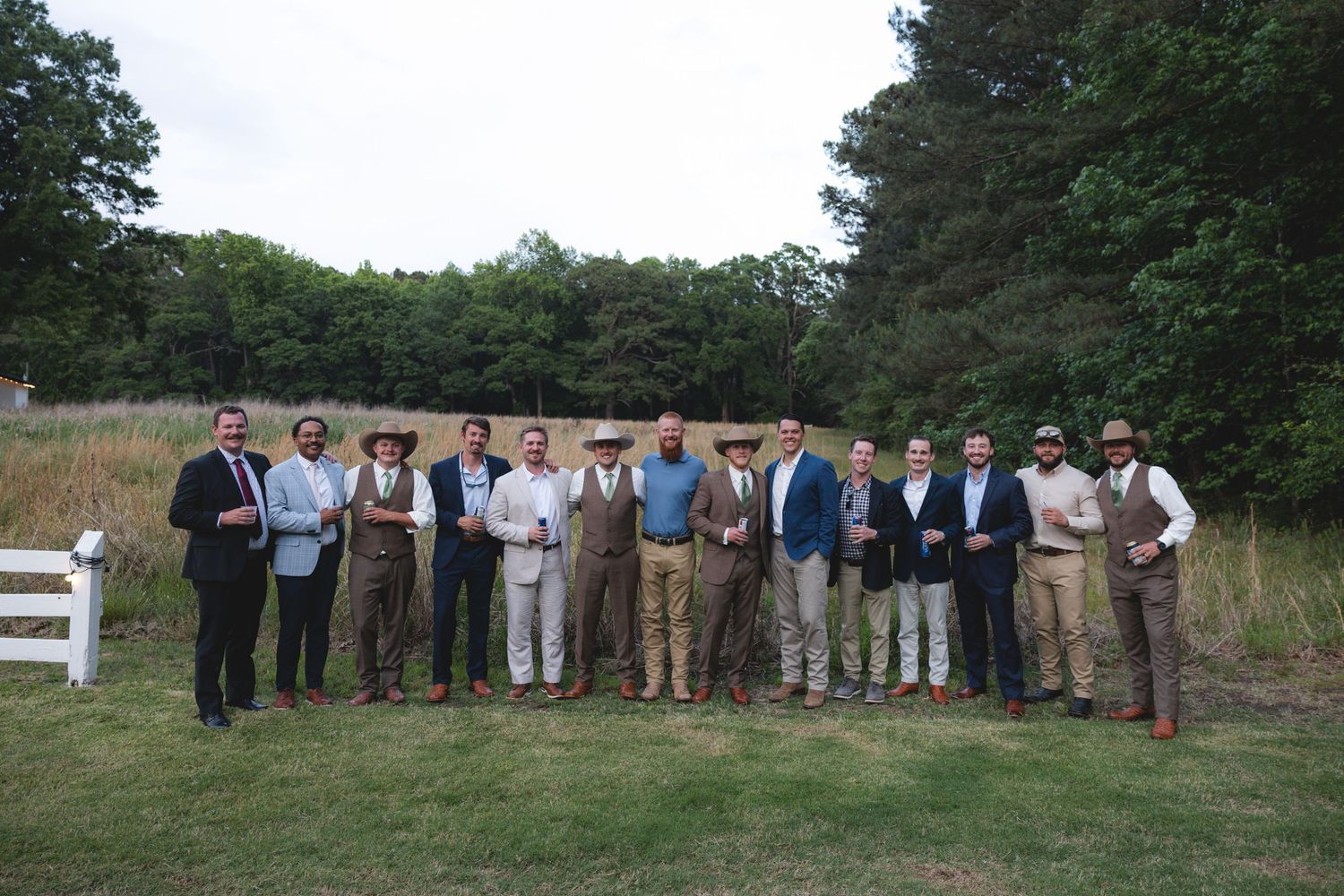 Group of well-dressed men posing outdoors in a field at a wedding celebration.