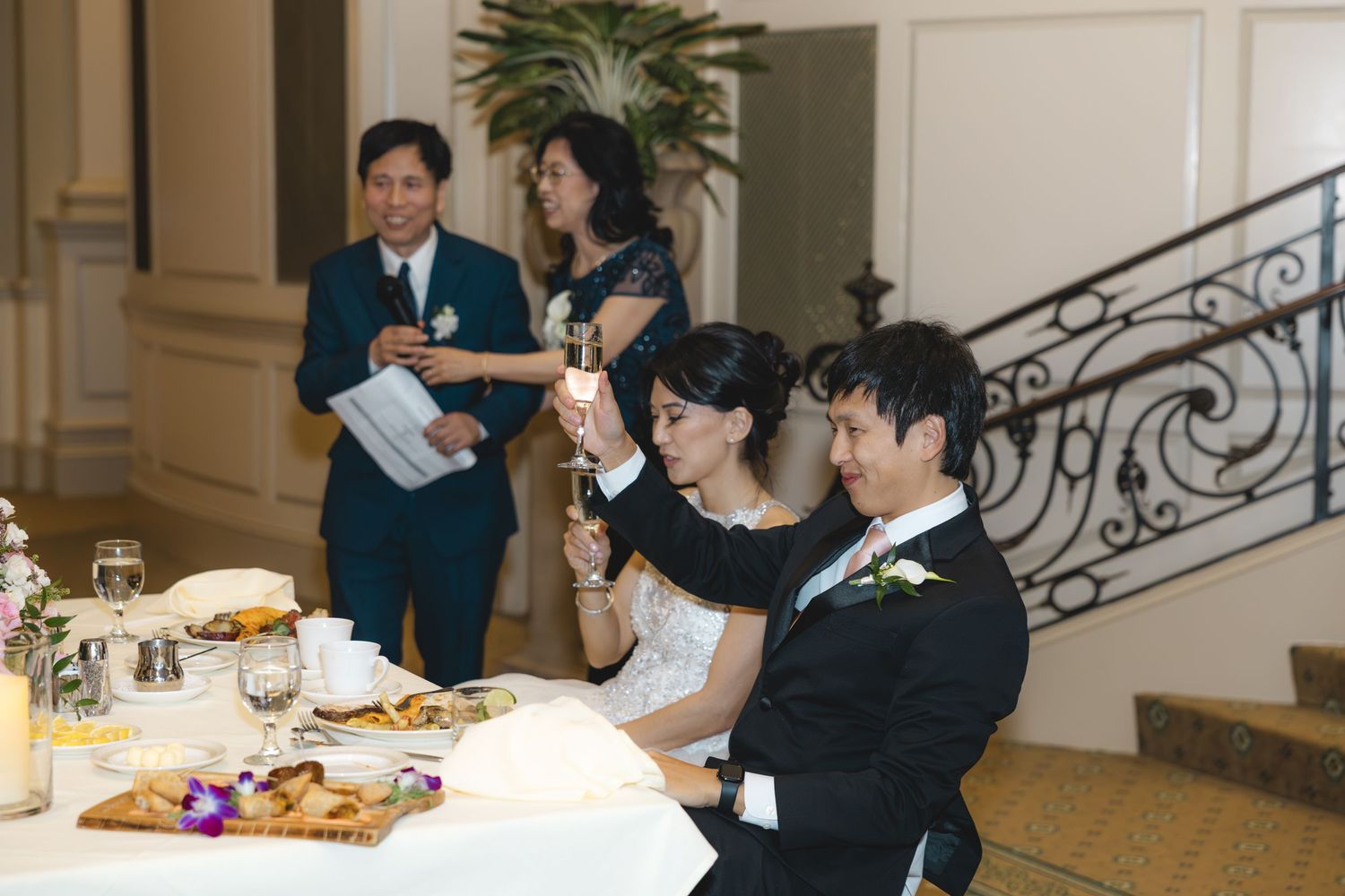 Bride and groom raising glasses for a toast during wedding reception speeches.