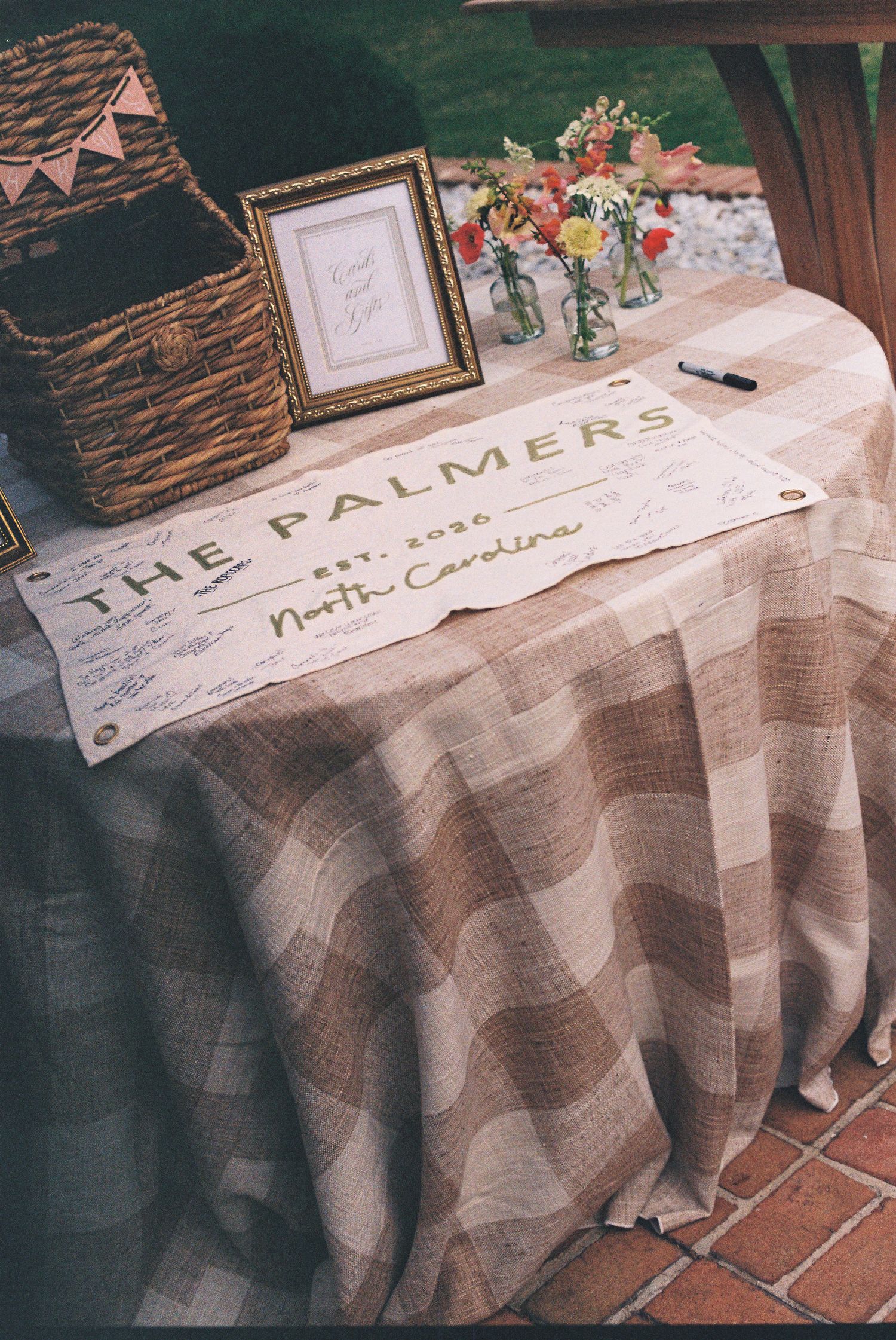 Rustic wedding guest table with The Palmers Est. 2020 North Carolina sign, wicker basket, and floral arrangement.