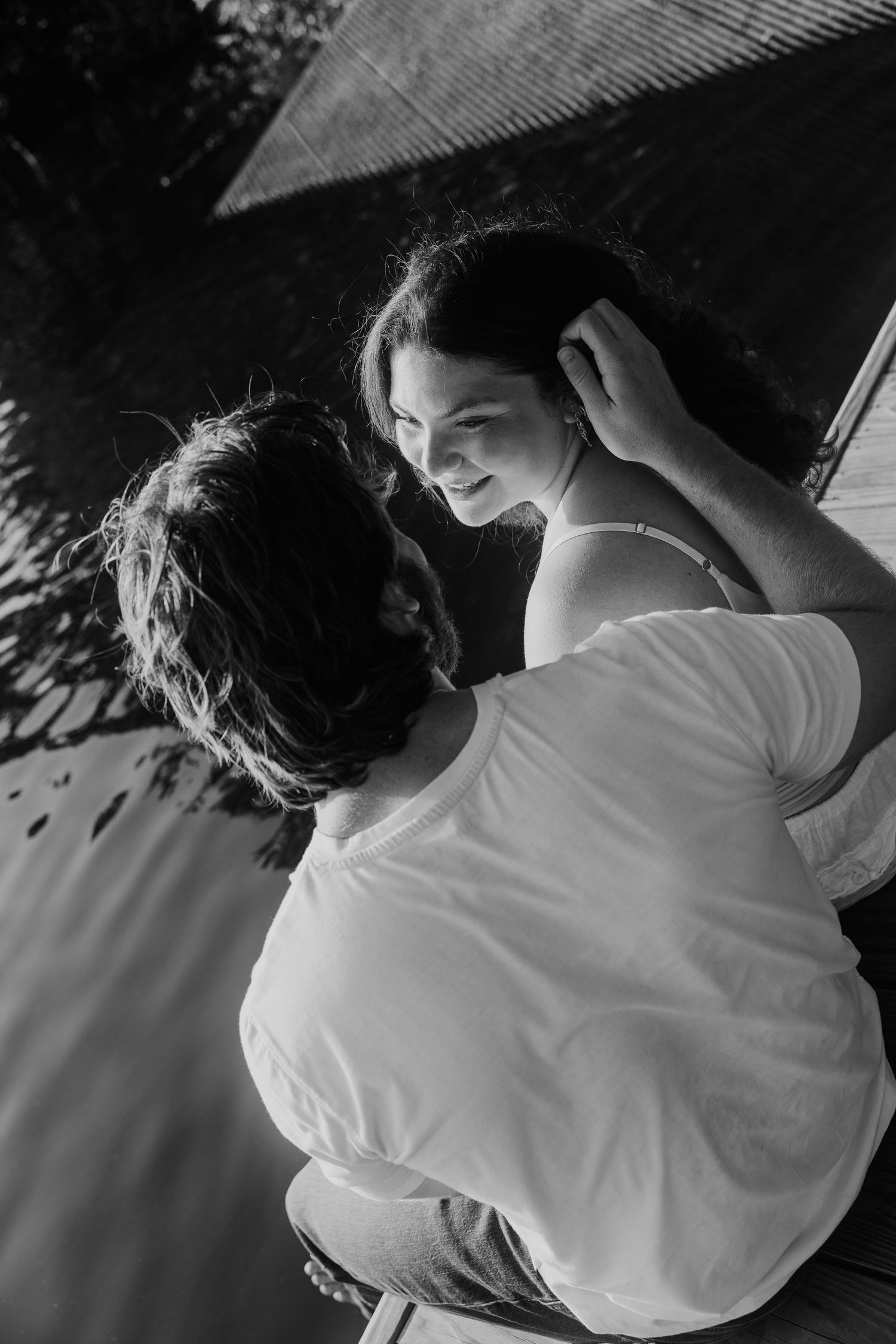 Black and white photo of a couple embracing outdoors, man gently touching womans hair as she smiles up at him.