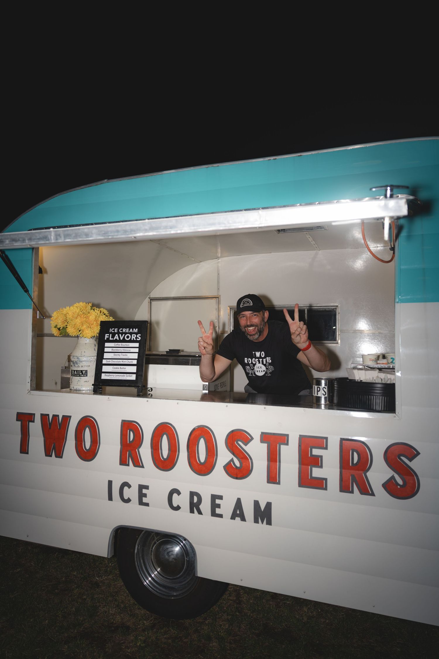 Cheerful vendor making peace signs inside the Two Roosters Ice Cream trailer.