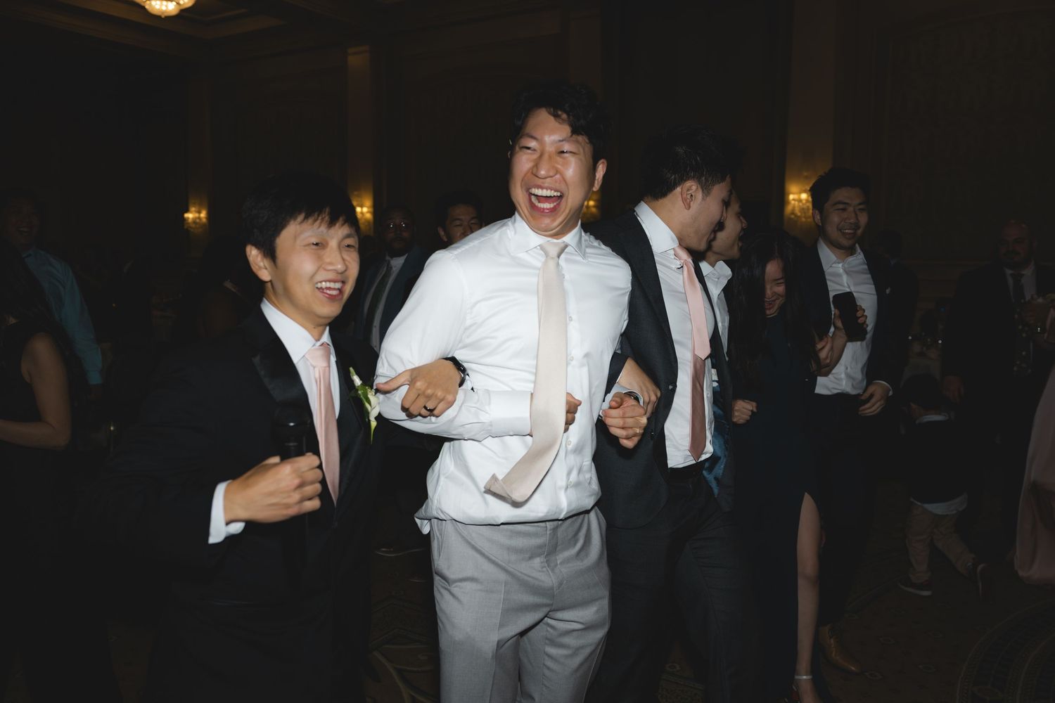 Joyful guests dancing and laughing at a wedding reception in a grand ballroom.