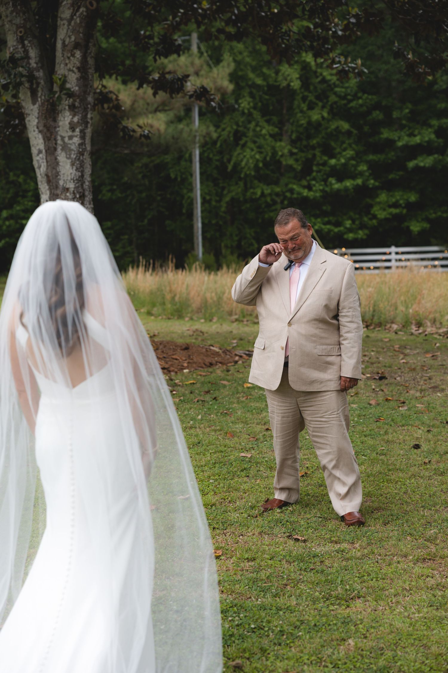 Emotional father wiping tears seeing bride daughter in white wedding gown and veil for first look.