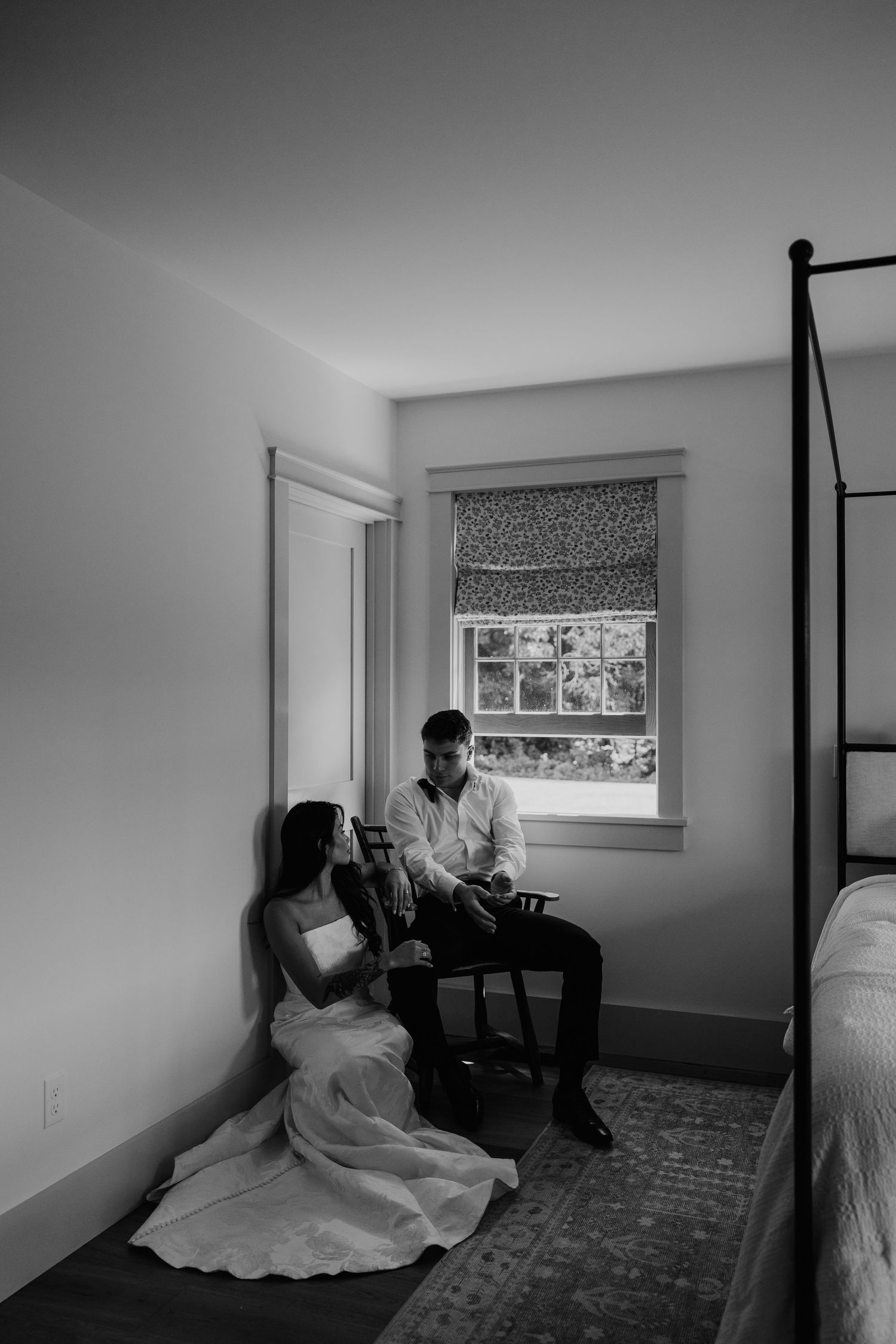 Black and white photo of bride and groom sharing a quiet moment in a sunlit bedroom corner on their wedding day.