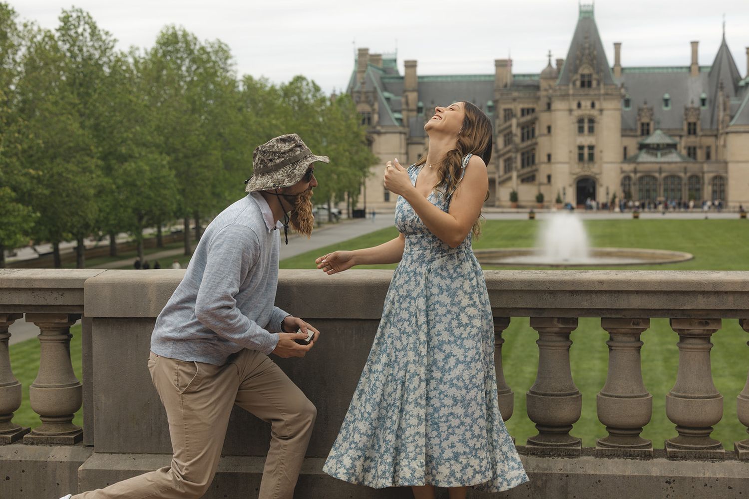 Couple sharing a joyful moment on a terrace with a fountain and grand estate in the background.