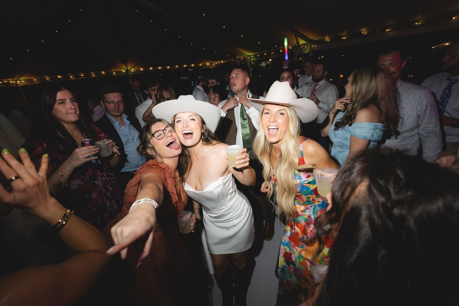 Three women in cowboy hats dancing and celebrating at a lively indoor party event.