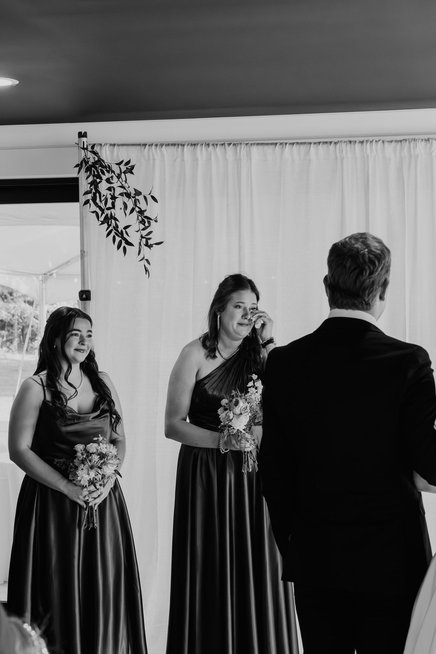 Black and white photo of two bridesmaids in dark gowns holding bouquets during a wedding ceremony.