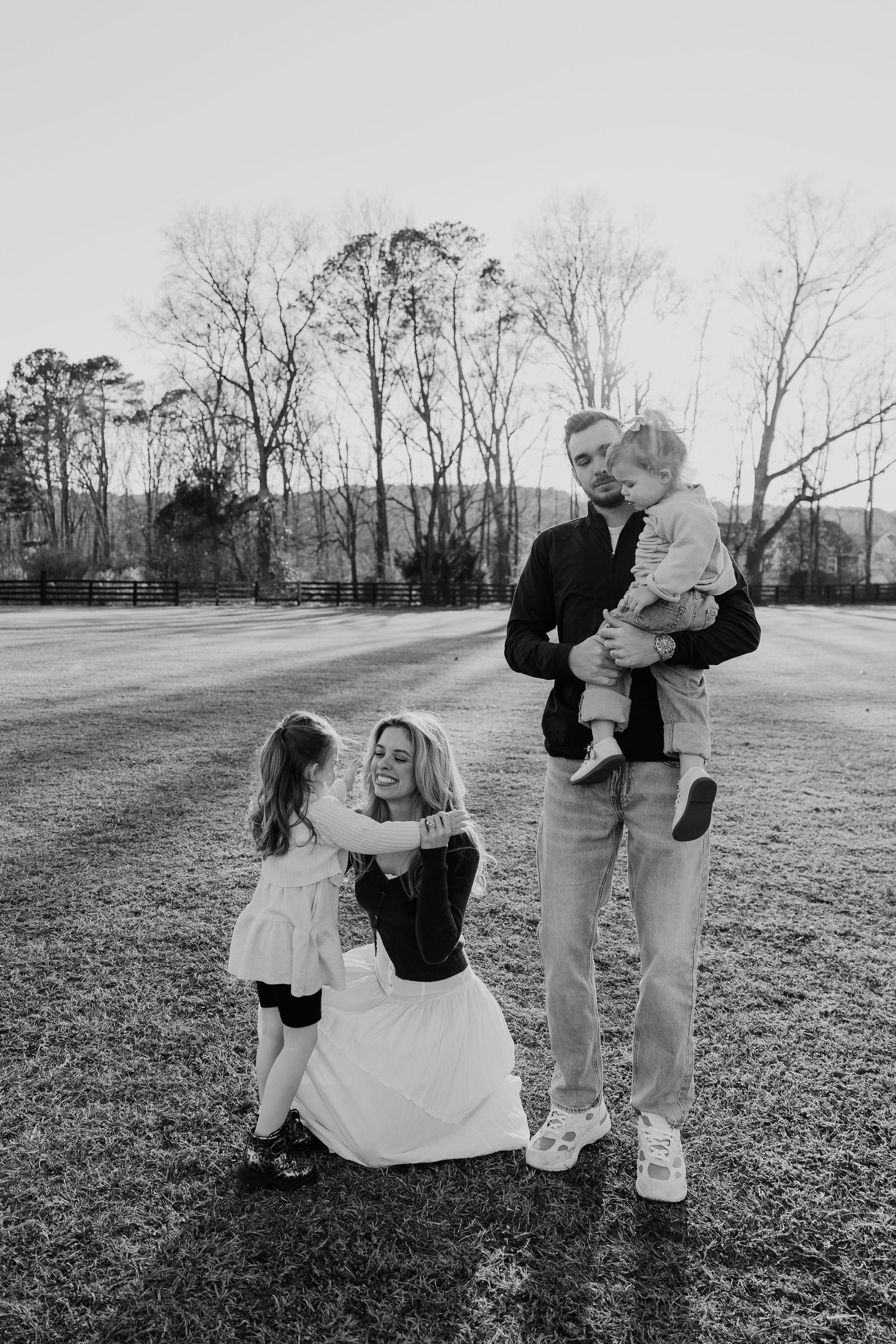 Black and white family portrait of parents with two young children in an open field.