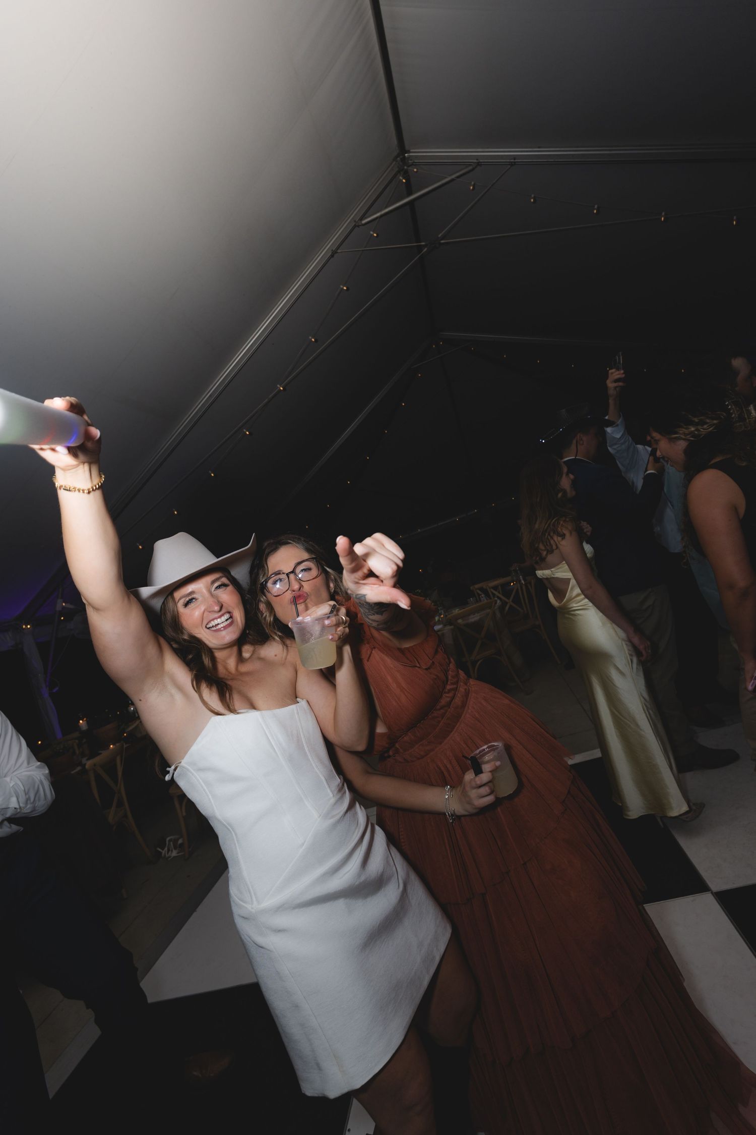 Two women dancing and taking selfies at a lively wedding reception party.