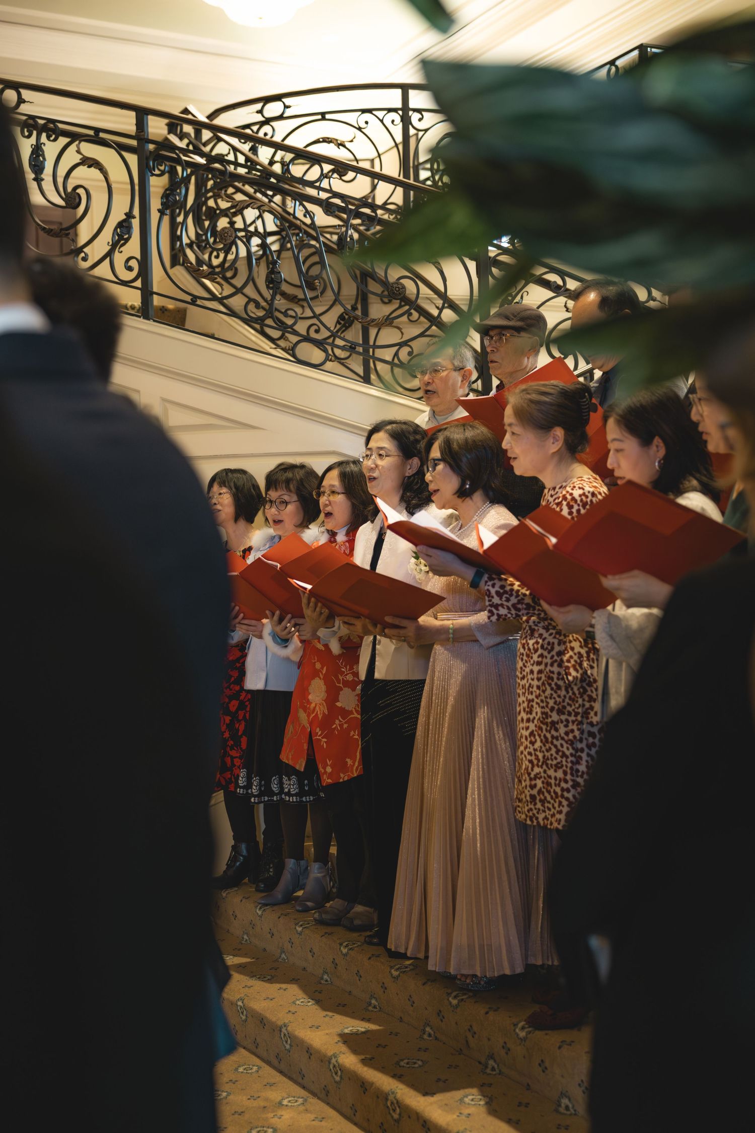 Wedding choir sings from red books on staircase during elegant indoor wedding ceremony.