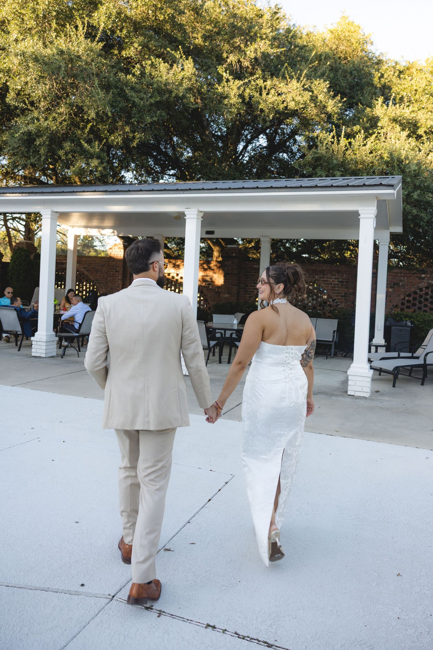Bride and groom walking hand in hand toward a white columned pavilion at an outdoor wedding venue.
