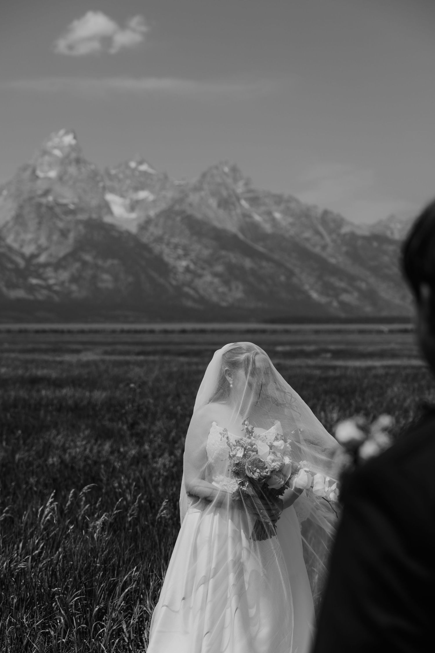 Black and white wedding photo of a bride in veil holding bouquet with Grand Teton mountains in background.