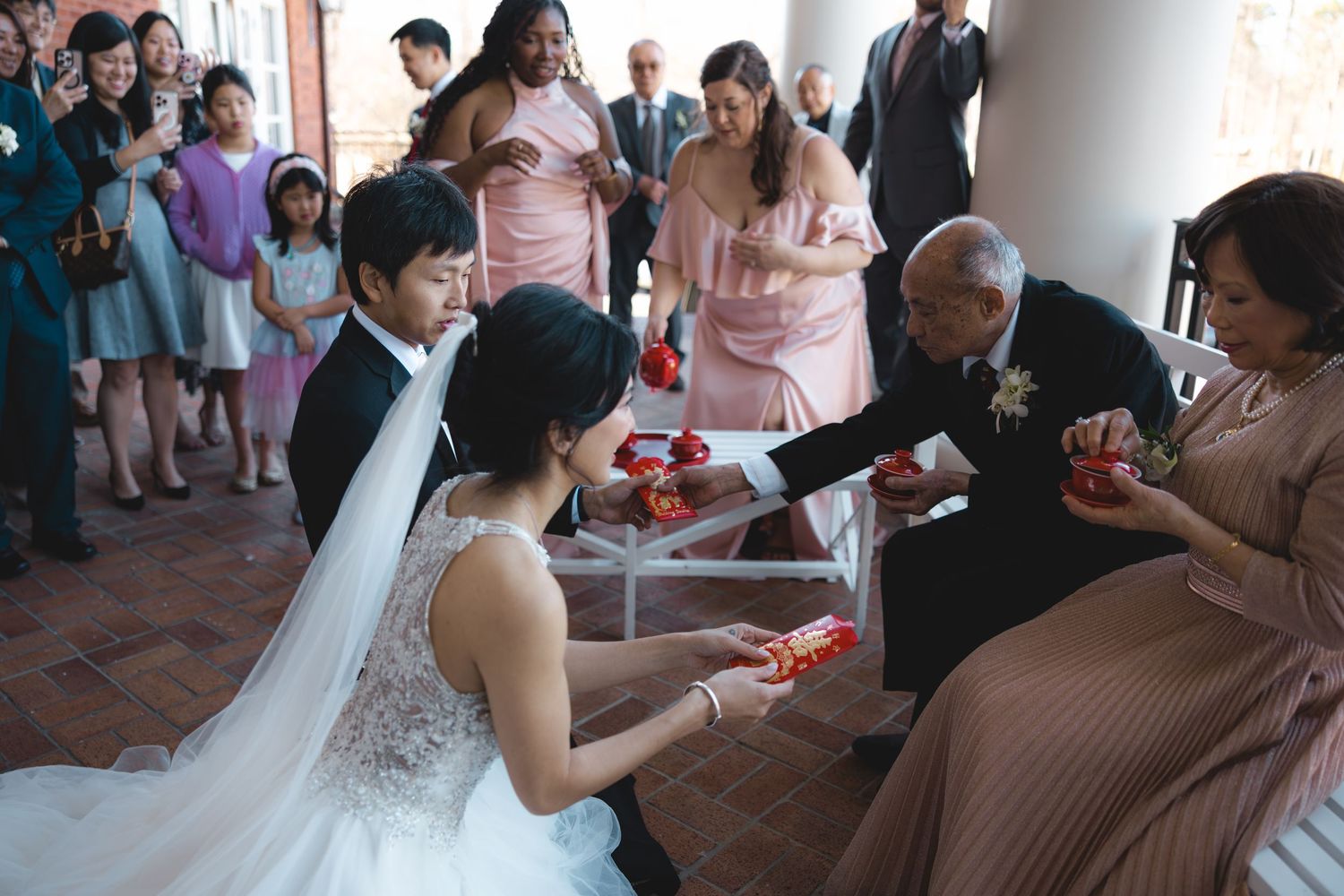 Asian bride and groom performing traditional Chinese tea ceremony with elderly family members.