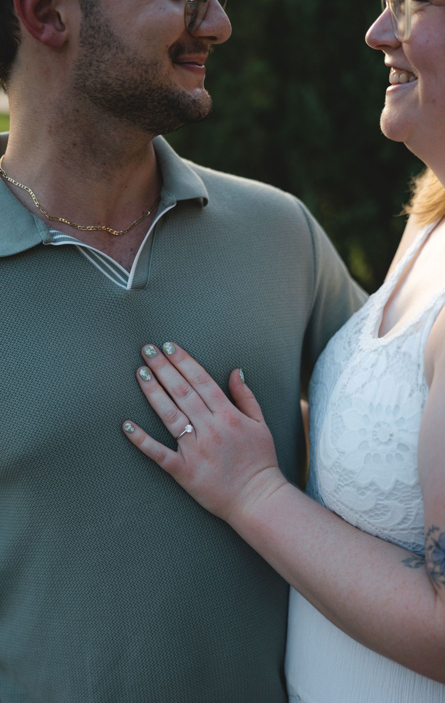 Couple smiling at each other, woman's hand with ring resting on man's chest wearing green polo shirt.