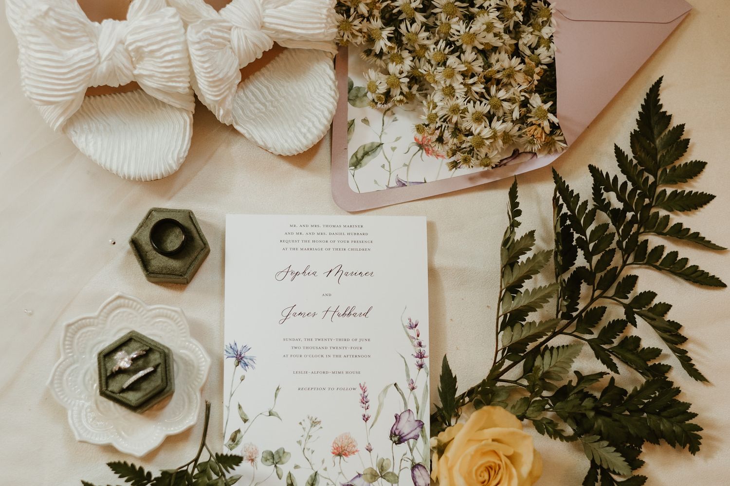A flat lay arrangement featuring wedding invitation, floral elements, and cozy slippers.