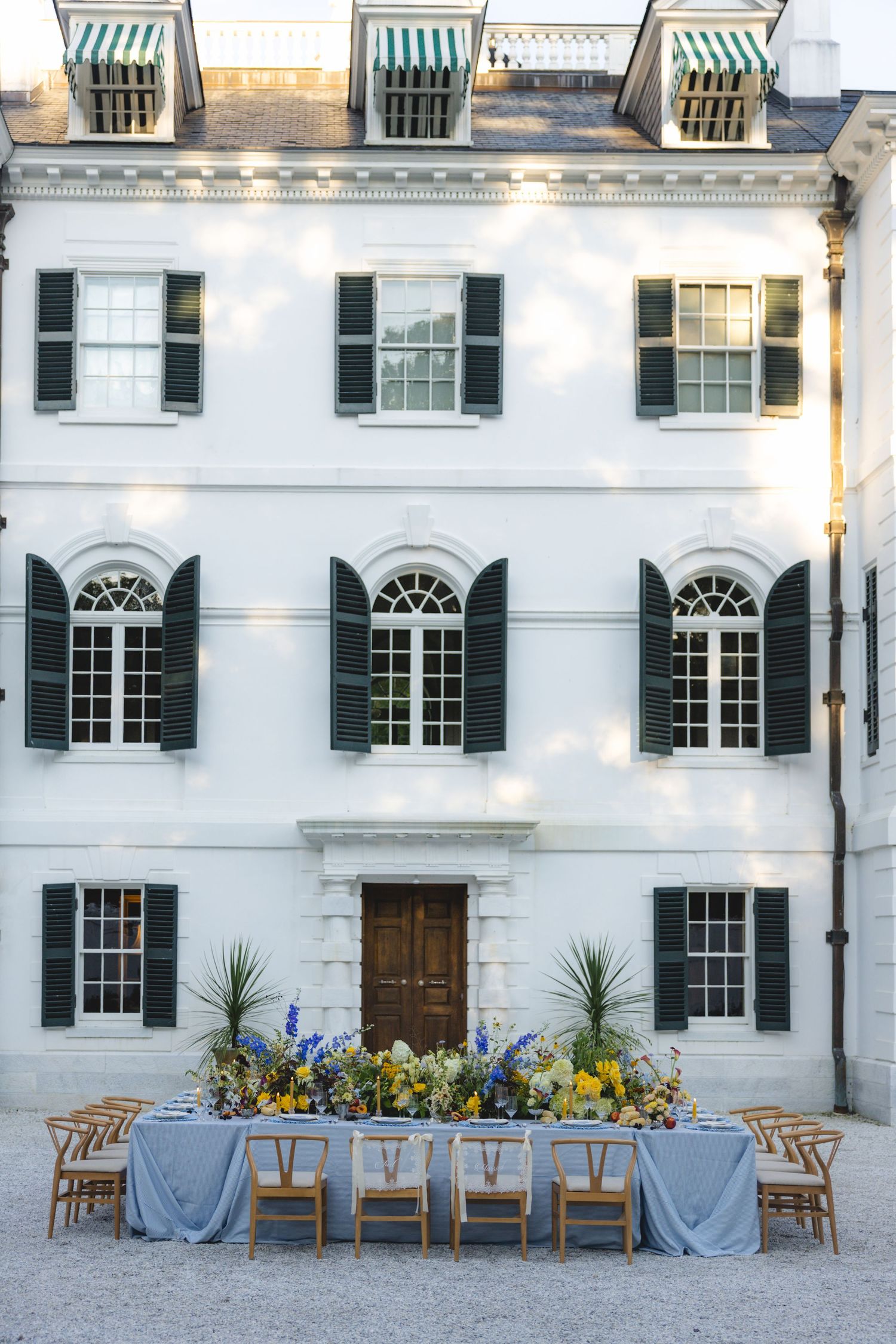 Elegant outdoor wedding reception table with yellow and blue florals set against a grand white Georgian mansion.