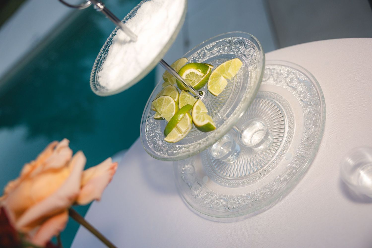 Crystal tiered dessert stand with fresh lime slices and ice near a pool, elegant party setup.