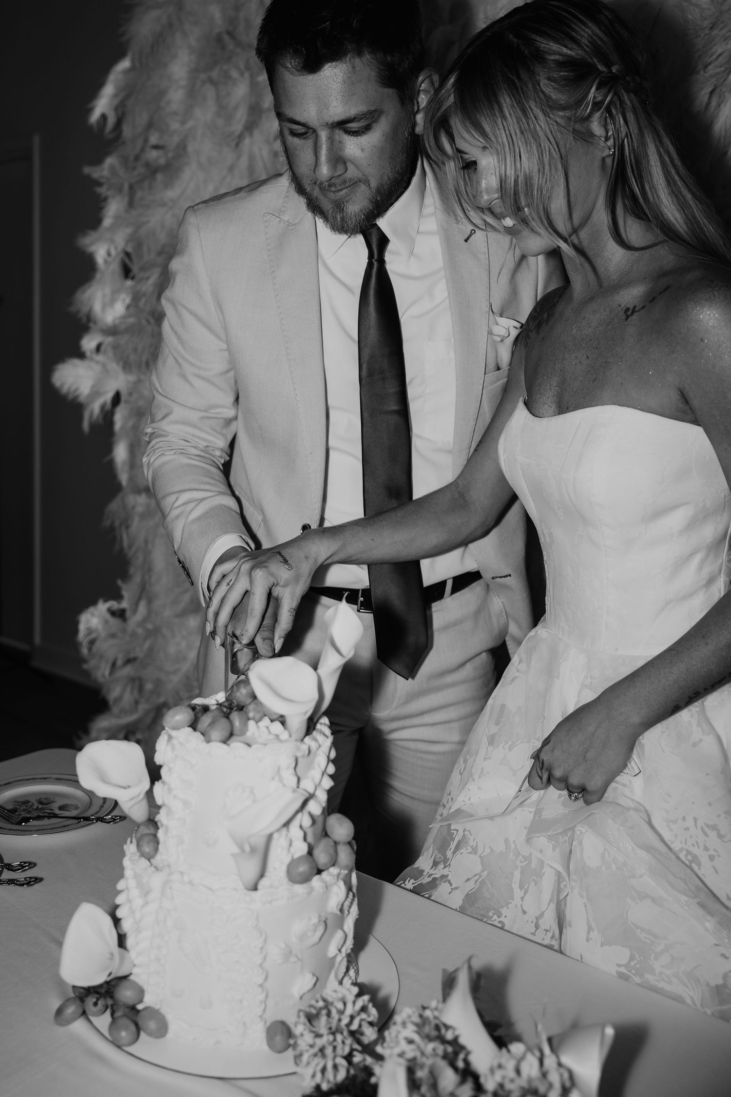 Black and white photo of bride and groom cutting wedding cake together at reception.