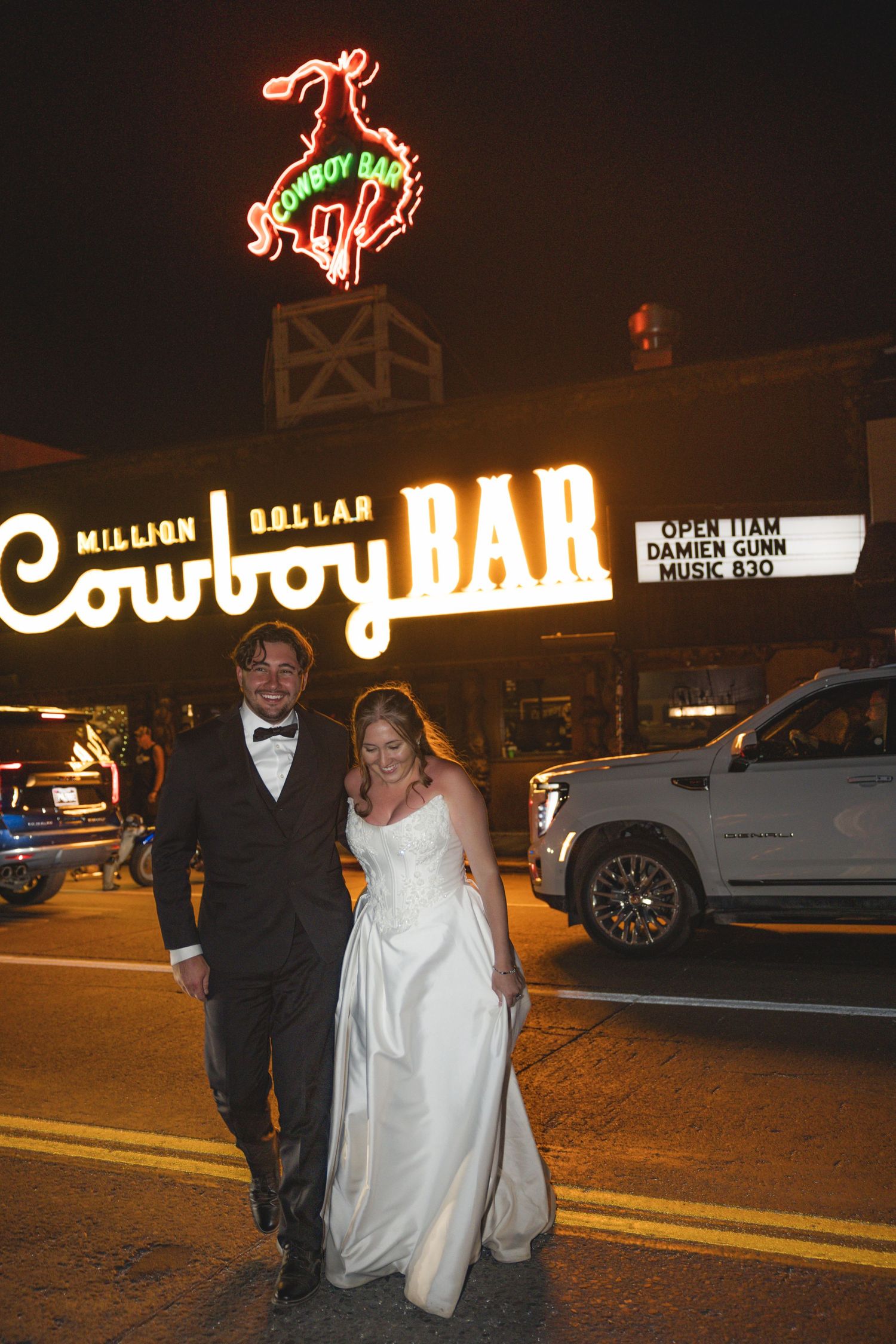 Newlywed couple posing in front of the Million Dollar Cowboy Bar neon sign at night in Jackson Hole.