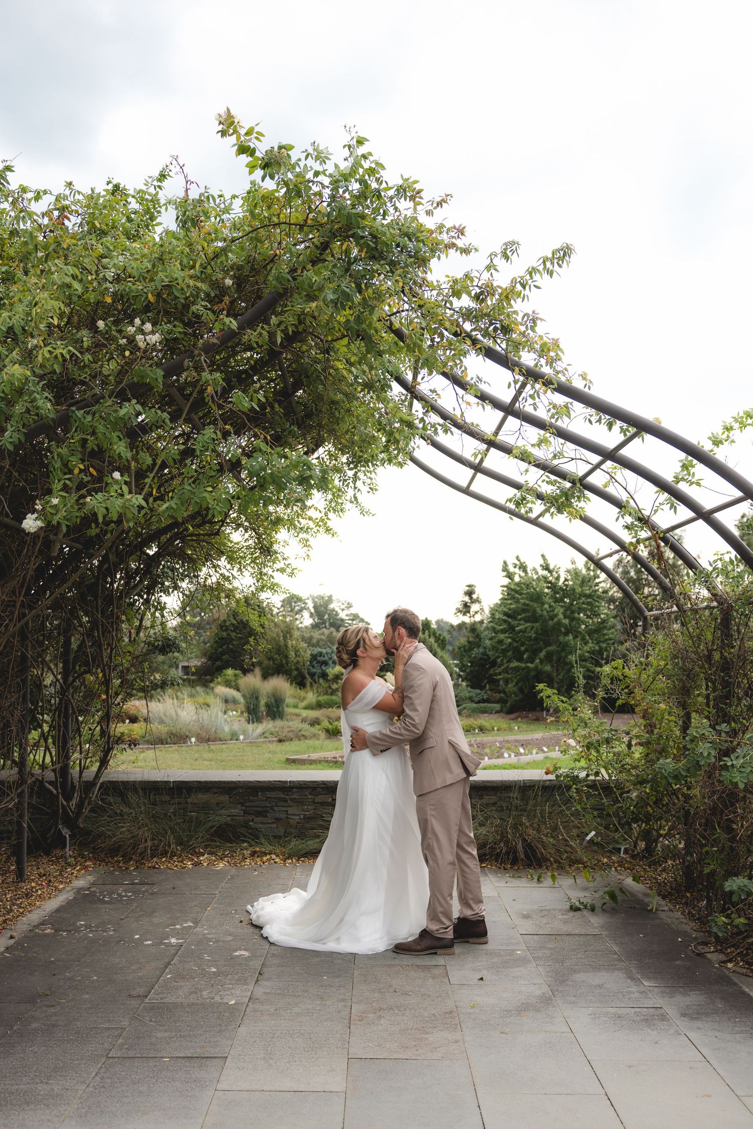 Bride and groom share a kiss under a lush garden arch on their wedding day.