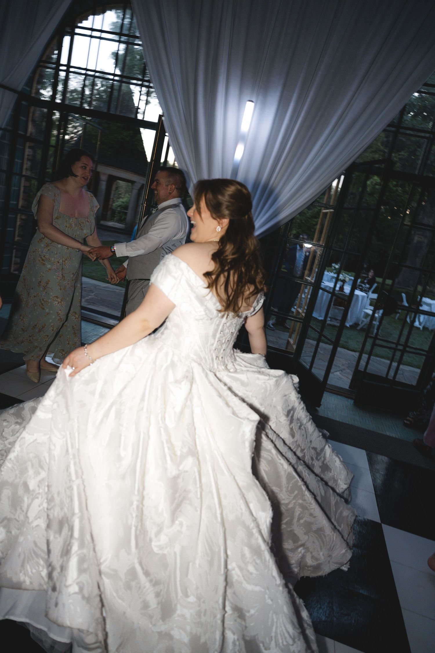 Bride in a flowing white ball gown dancing gracefully on a checkered dance floor at an elegant wedding reception.