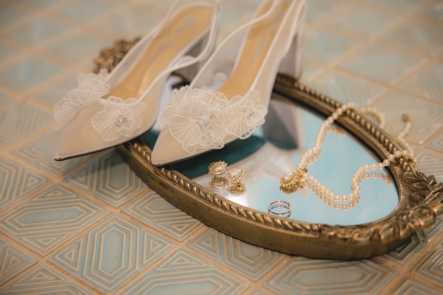 Elegant white bridal heels with lace details displayed on a decorative tray with pearl and gold jewelry.