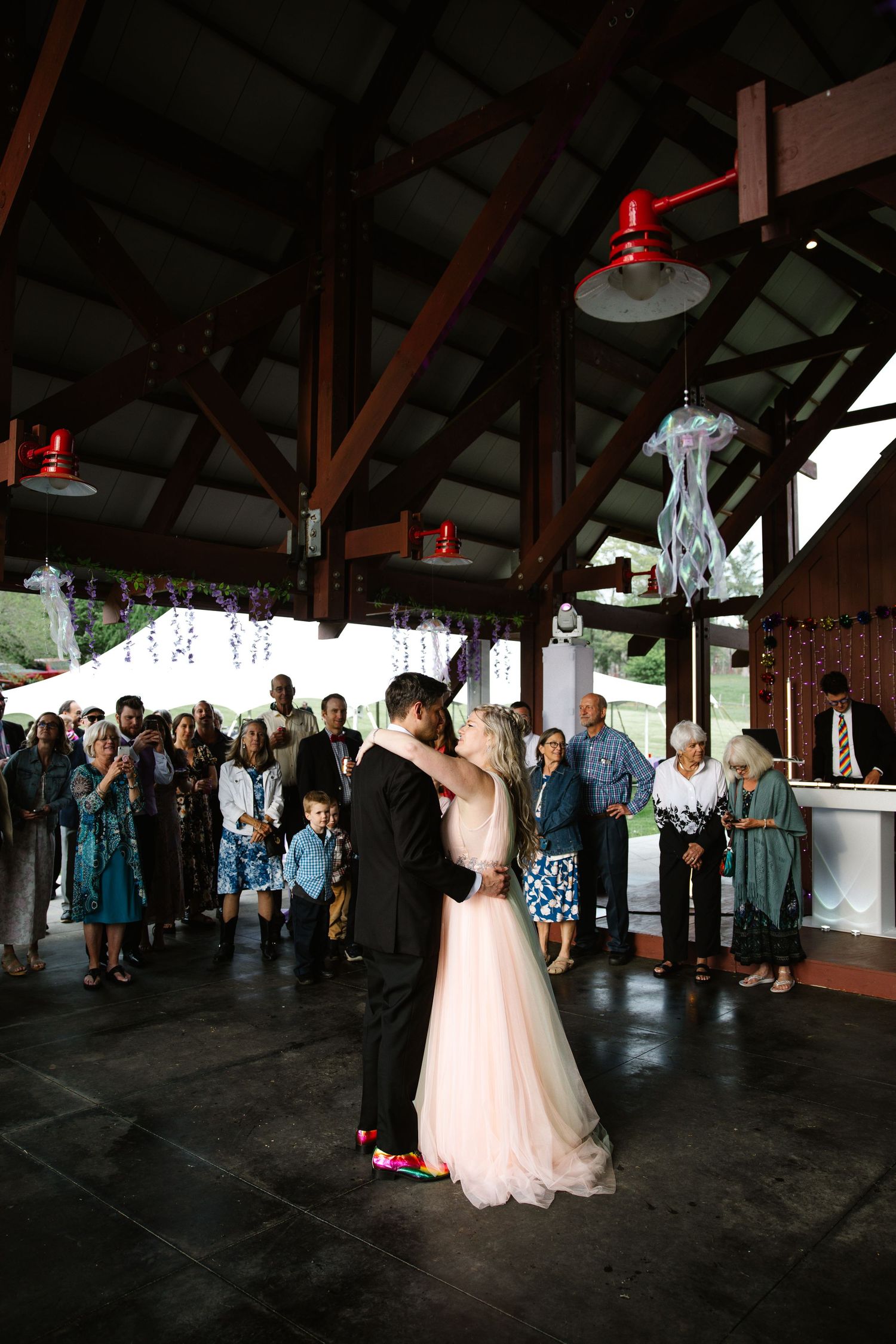 First dance at wedding reception with guests watching in rustic venue with exposed beams.