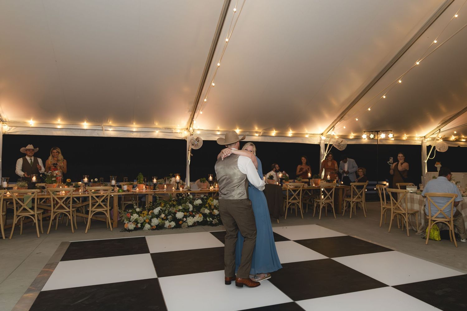 Newlywed couple shares first dance on black and white checkered floor at a romantic tented wedding reception.