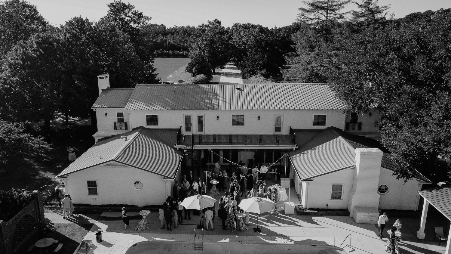 Aerial black and white view of a charming venue with guests gathering under umbrellas outside a historic building.