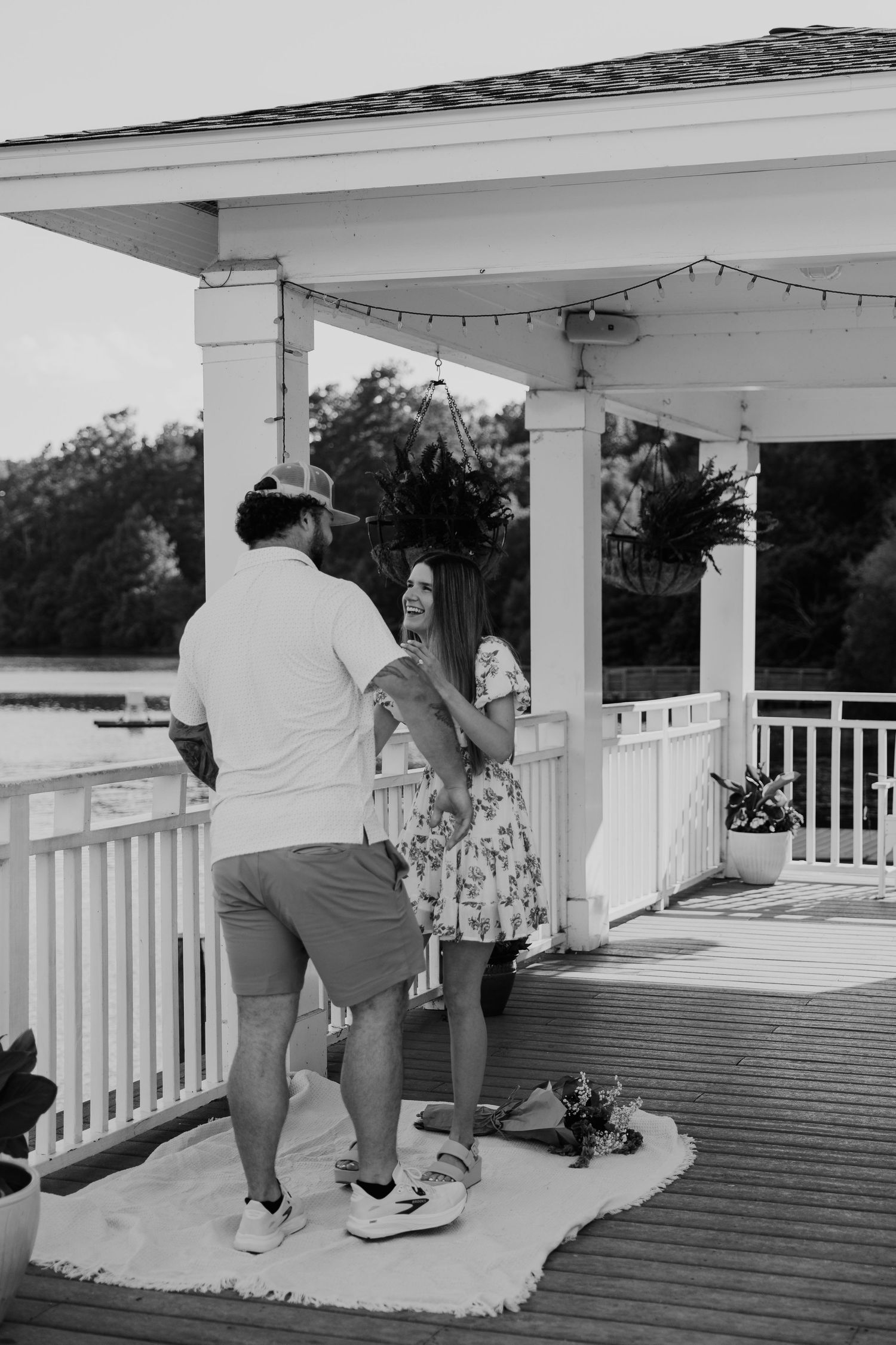 Black and white photo of a couple sharing a romantic moment on a decorated waterfront gazebo deck.