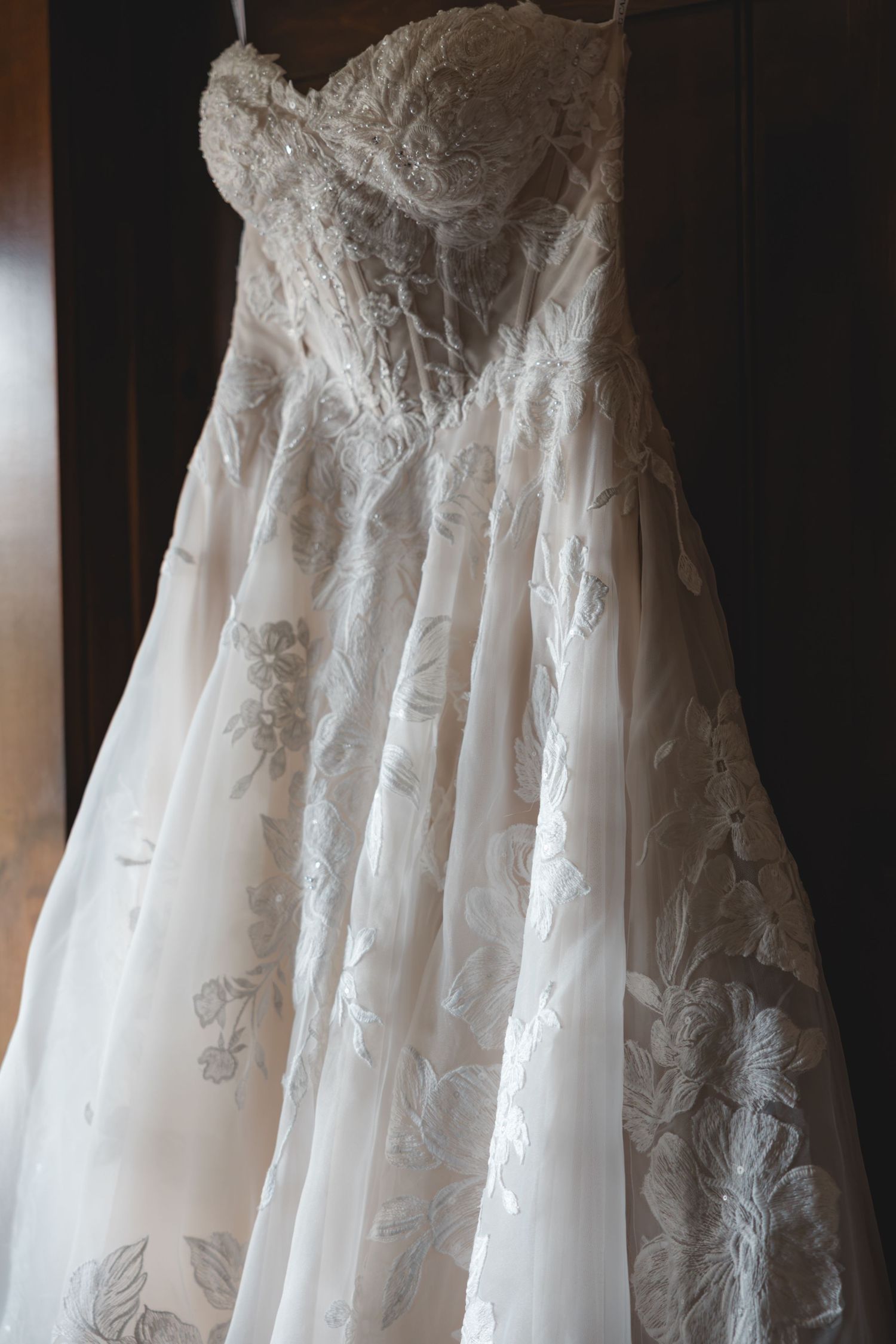 Elegant strapless lace wedding dress with floral embroidery hanging on display, featuring a sweetheart neckline.